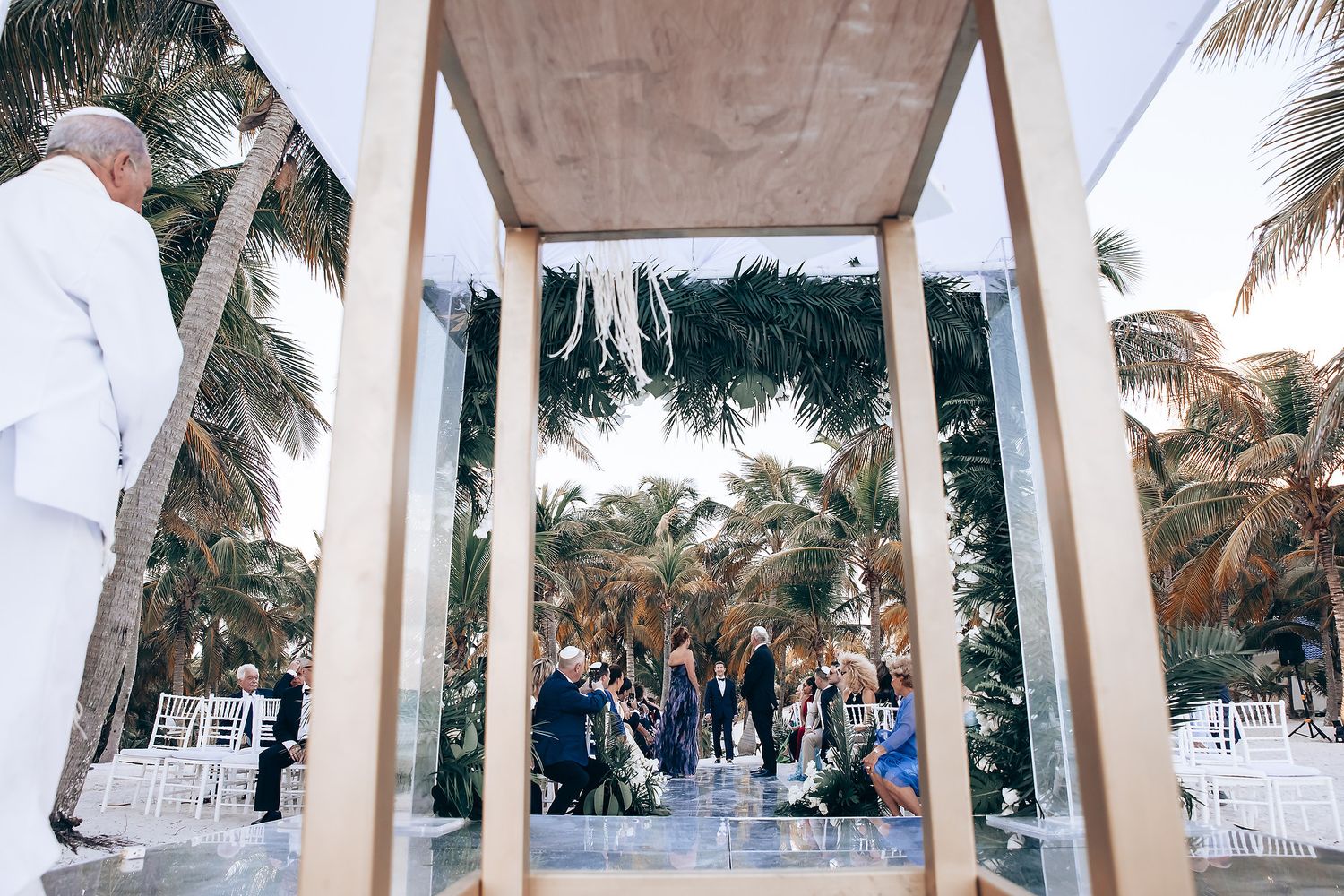 Outdoor wedding venue with white pillars and palm trees framing the scene.