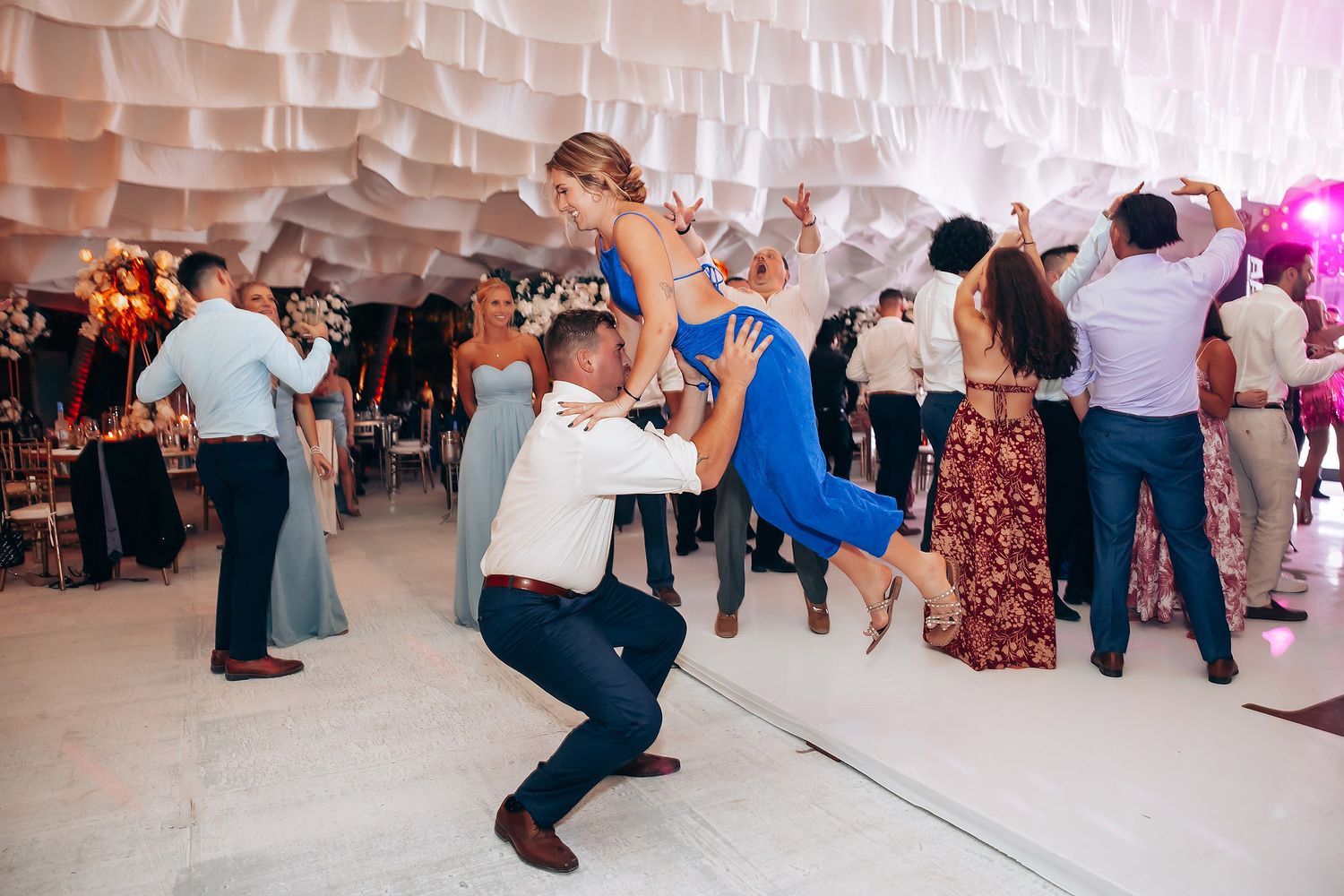 Wedding guests dancing and celebrating on the dance floor under white draped ceiling.