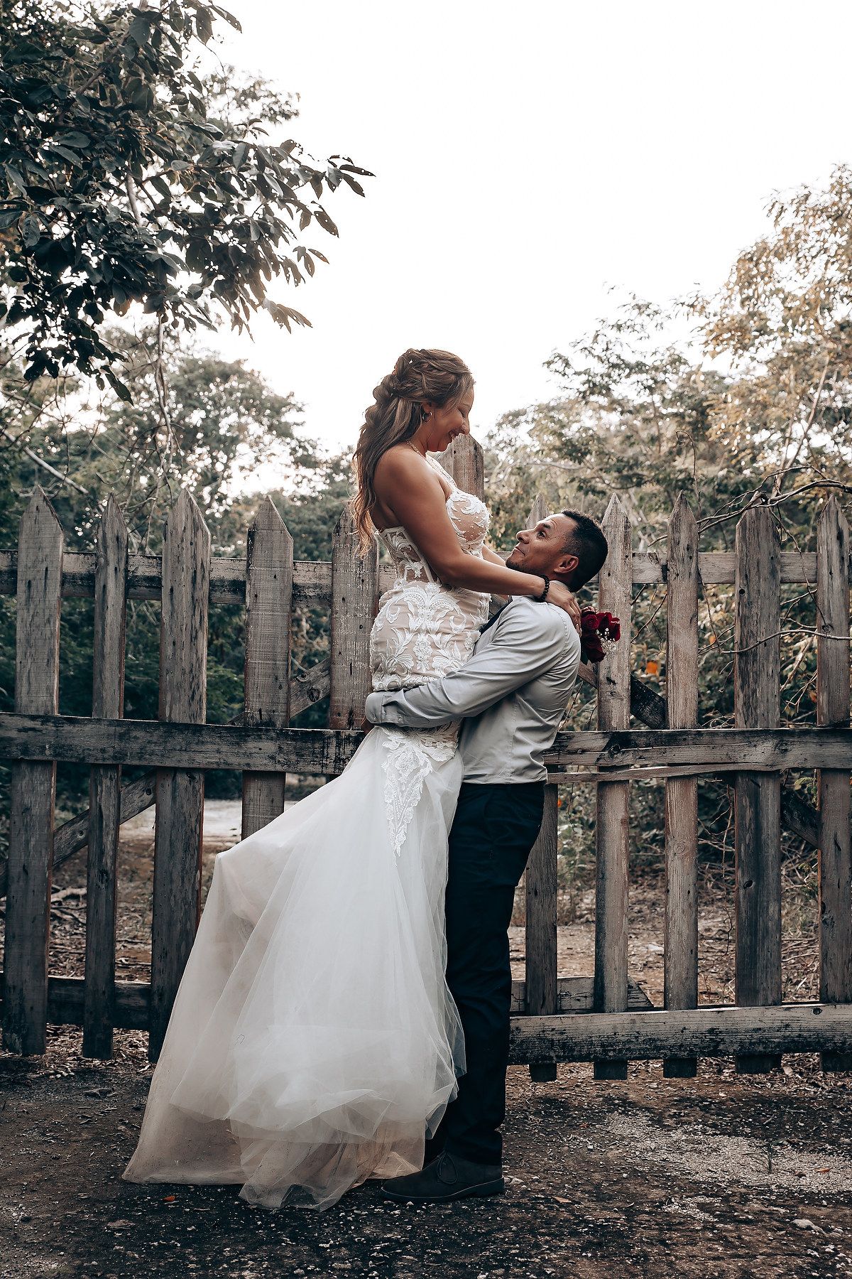 A romantic wedding photoshoot by a rustic wooden fence in a garden setting.