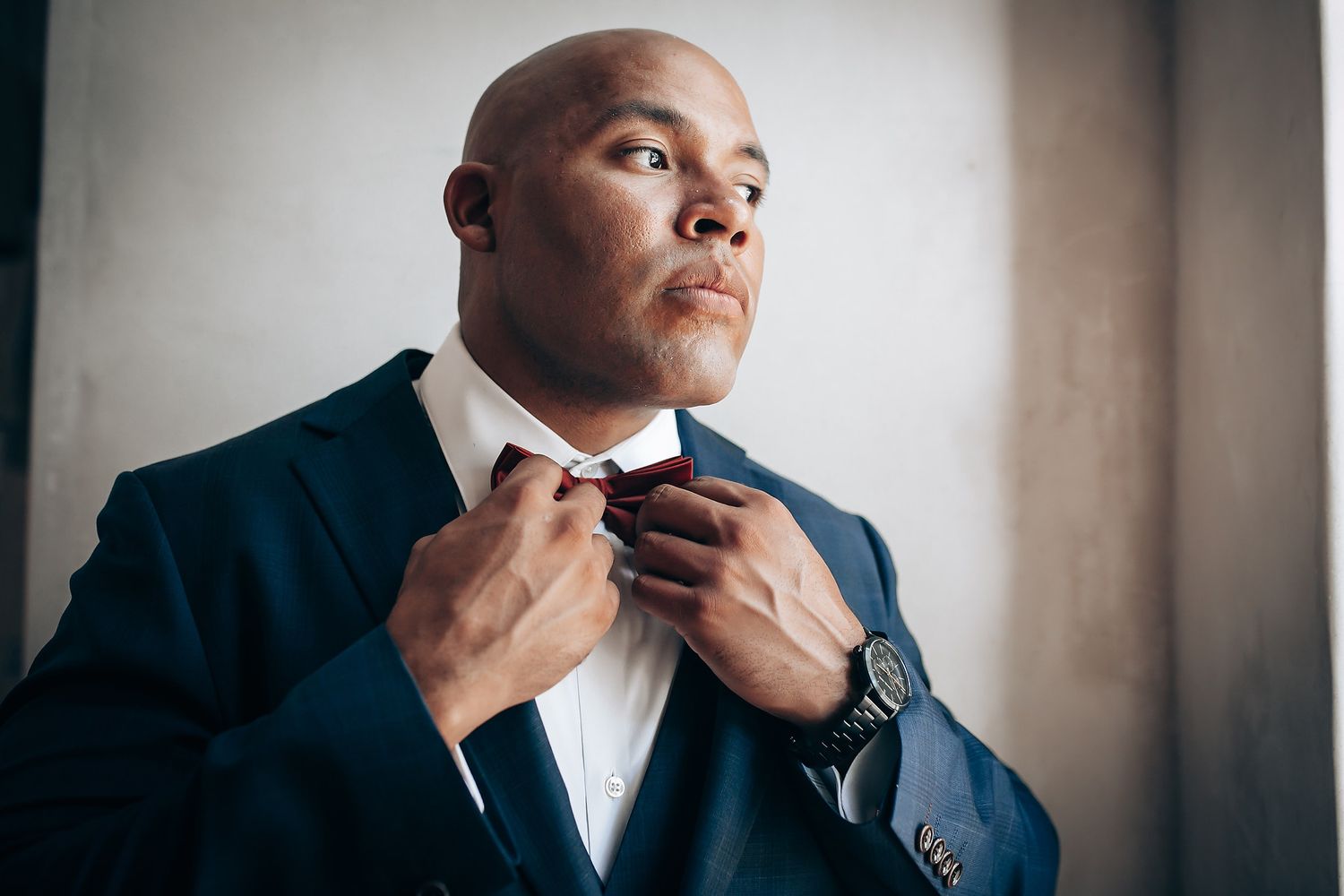 Person in navy suit adjusts tie while preparing for formal event.