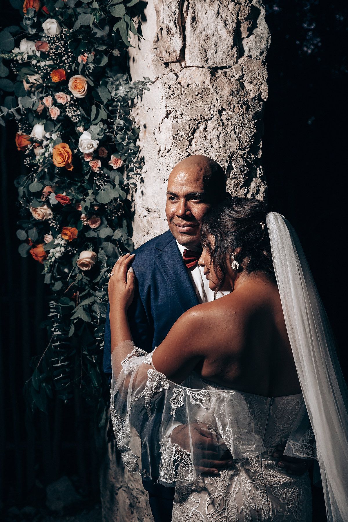 Intimate wedding portrait under stone archway with floral decorations.