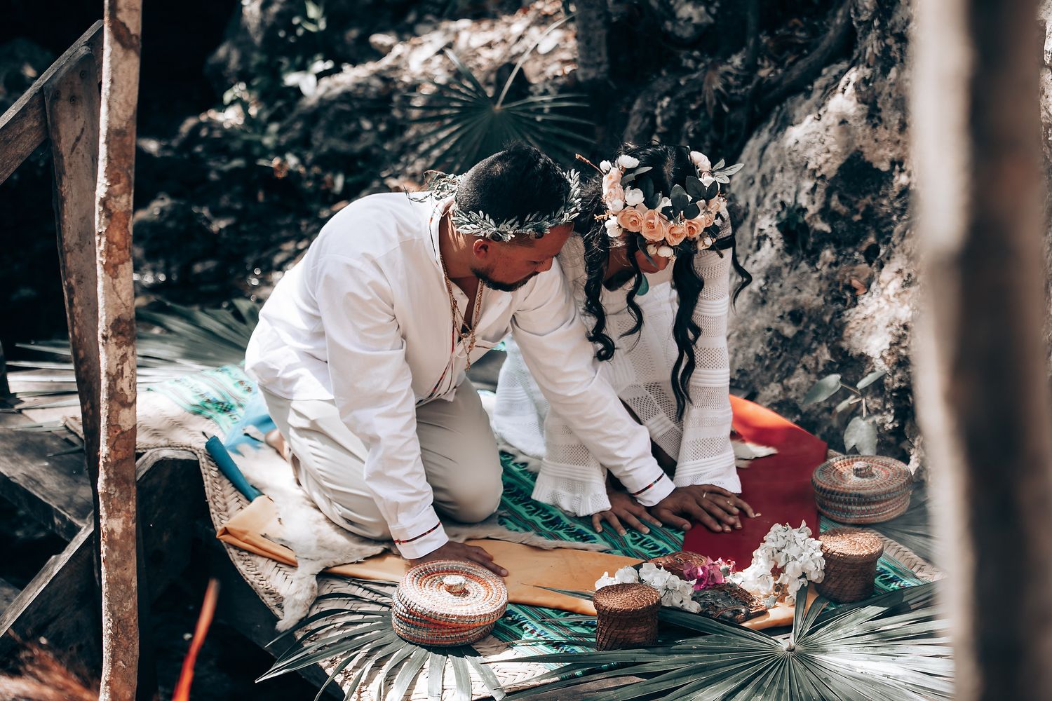People seated on the ground in white attire during an outdoor forest gathering.