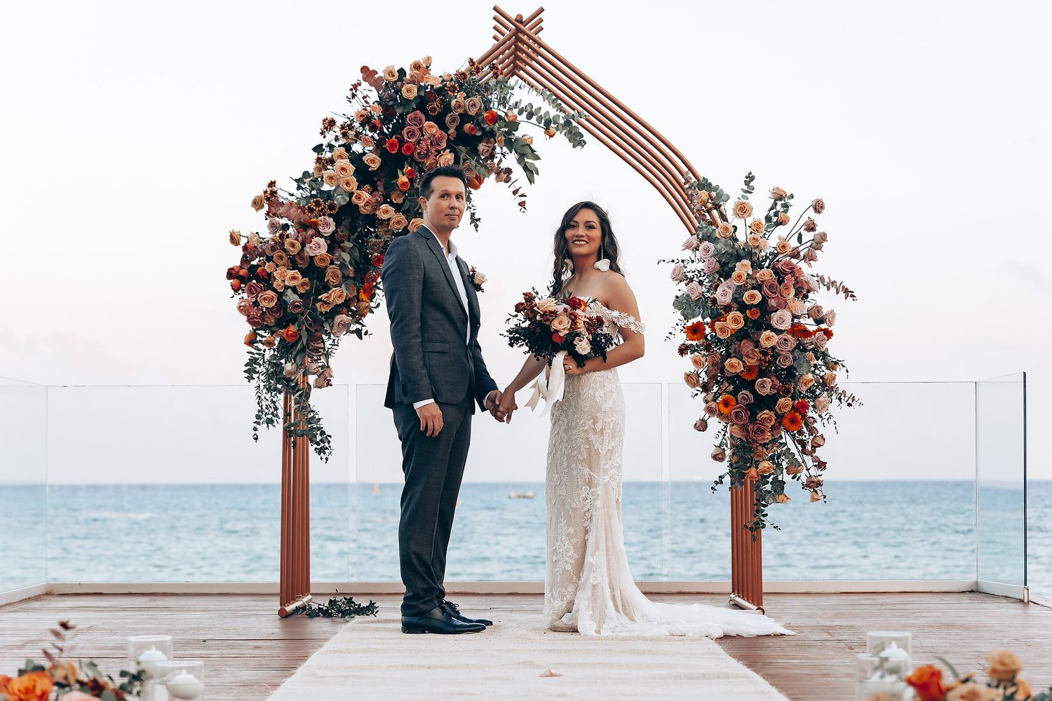 Oceanfront wedding ceremony setup with coral floral arches and white chairs.