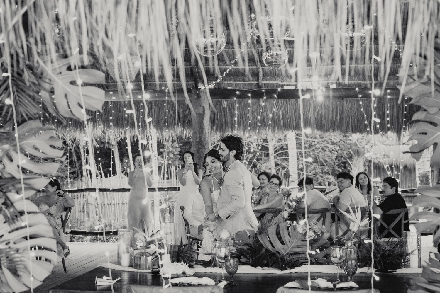 Black and white photo of a wedding ceremony under decorated tent with streamers and floral arrangements.