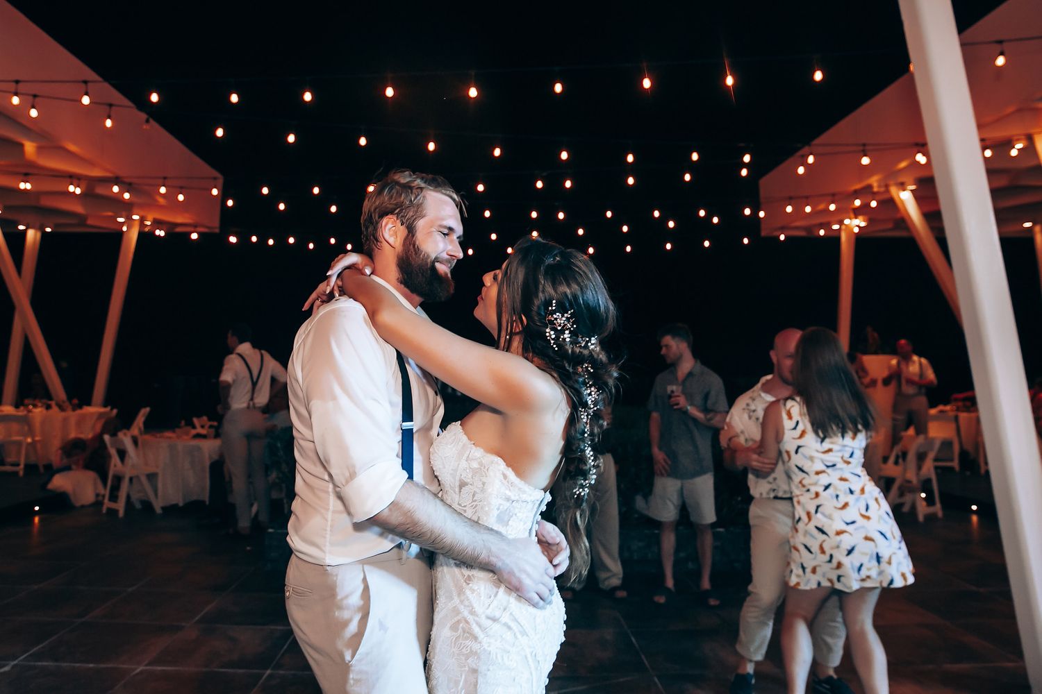 Wedding reception dance under twinkling lights at night with guests celebrating.