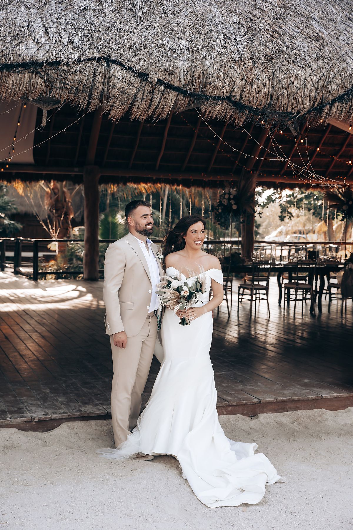 Couple shares their first dance under a rustic thatched-roof pavilion at a tropical beach wedding reception.