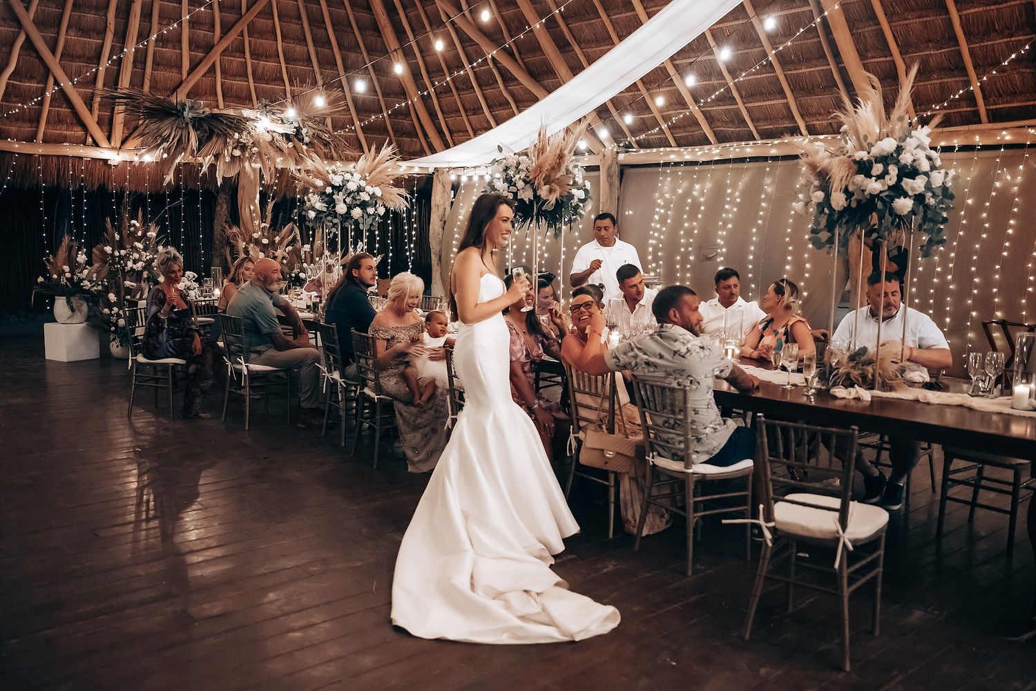 Newlyweds perform their first dance surrounded by guests in an elegantly decorated barn reception space.