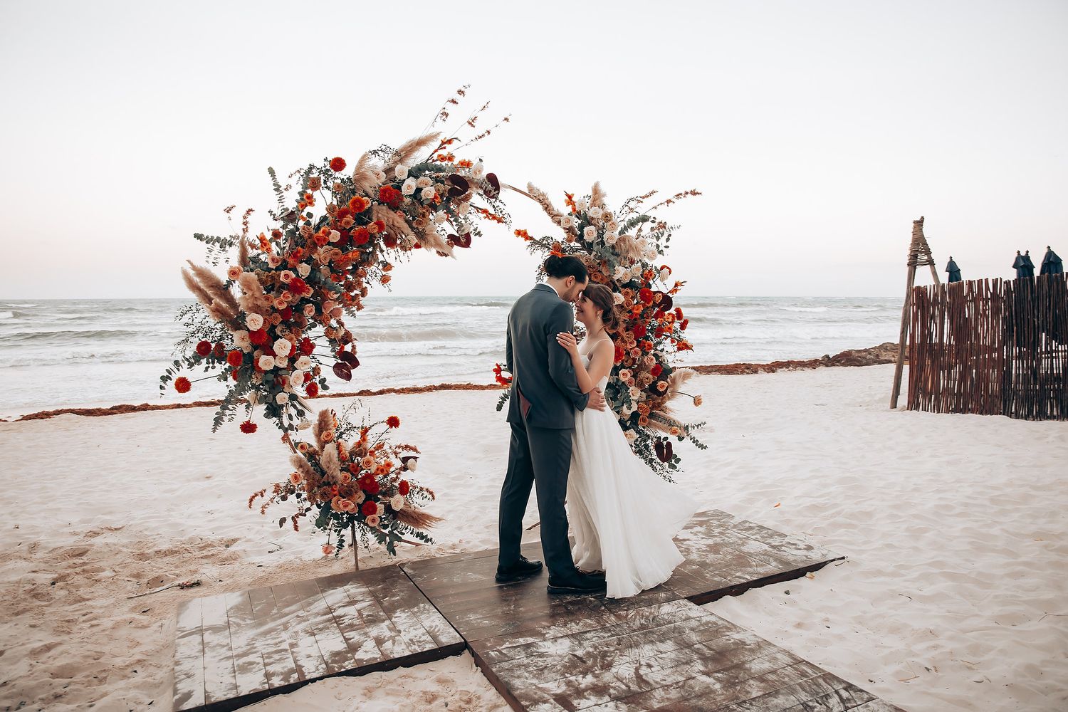 Beachfront wedding ceremony setup with dramatic red floral arrangements on white sand.