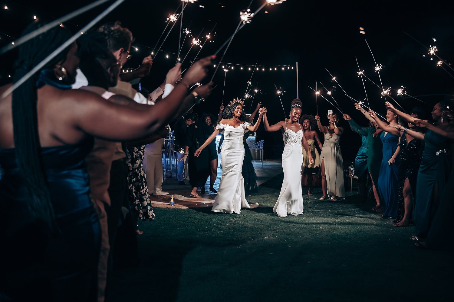 Nighttime wedding reception under string lights with guests celebrating.