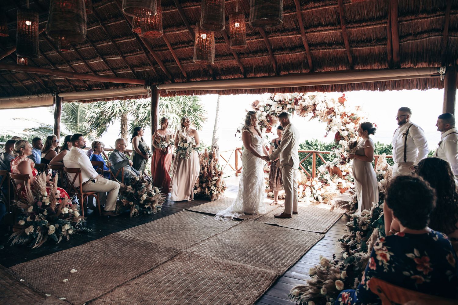 Couple exchanging vows at a rustic outdoor wedding ceremony with floral arch.