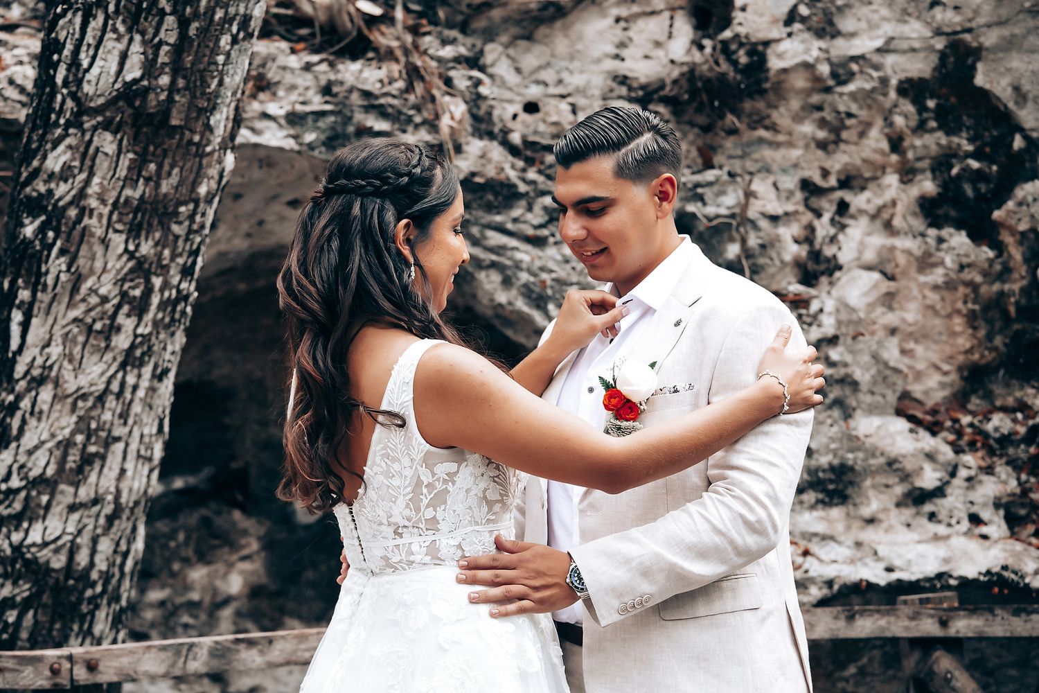 A romantic wedding couple embraces against a rocky backdrop in elegant white attire.