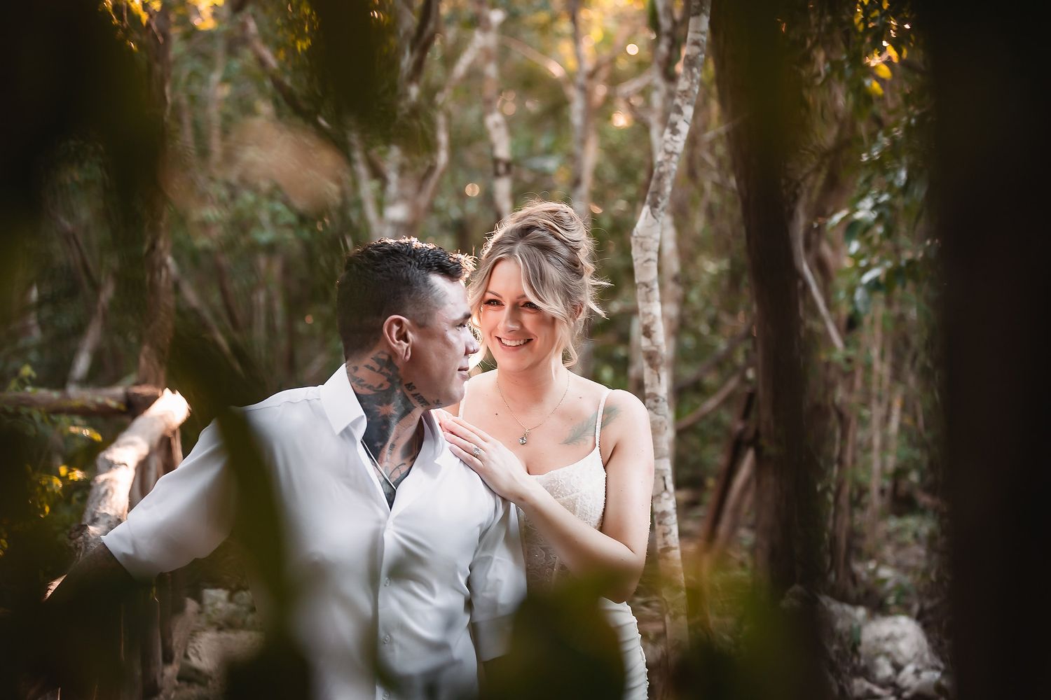 Couple sharing a romantic moment surrounded by lush forest trees in wedding attire.