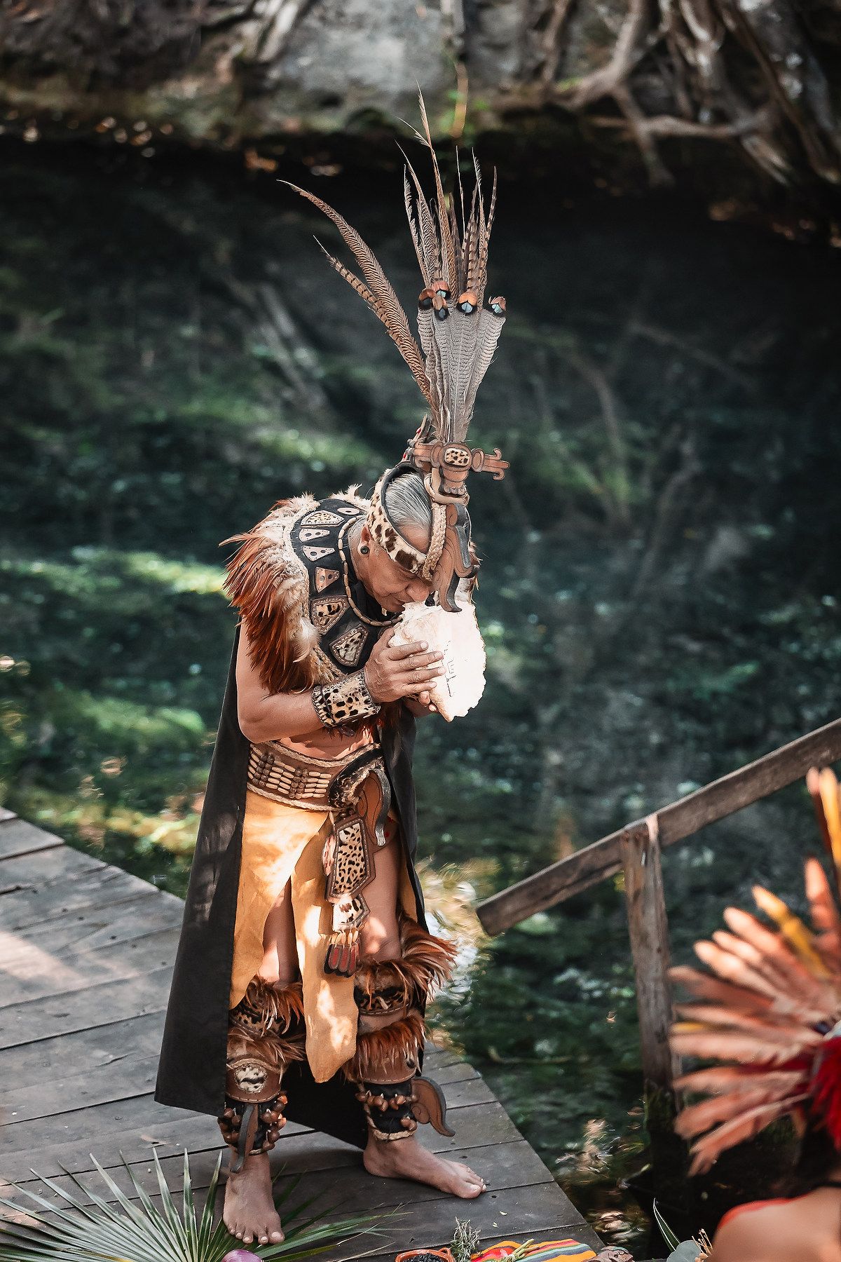 Mayan warrior in traditional ceremonial costume with feathered headdress performing ritual at cenote in Mexico.