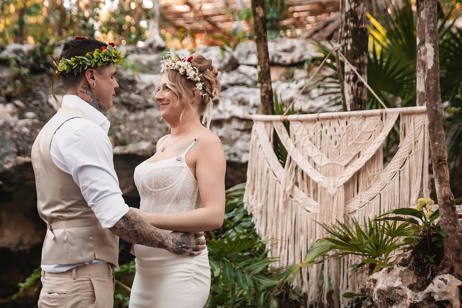 Bride and groom exchange vows outdoors with macrame backdrop and tropical greenery in a boho wedding ceremony.