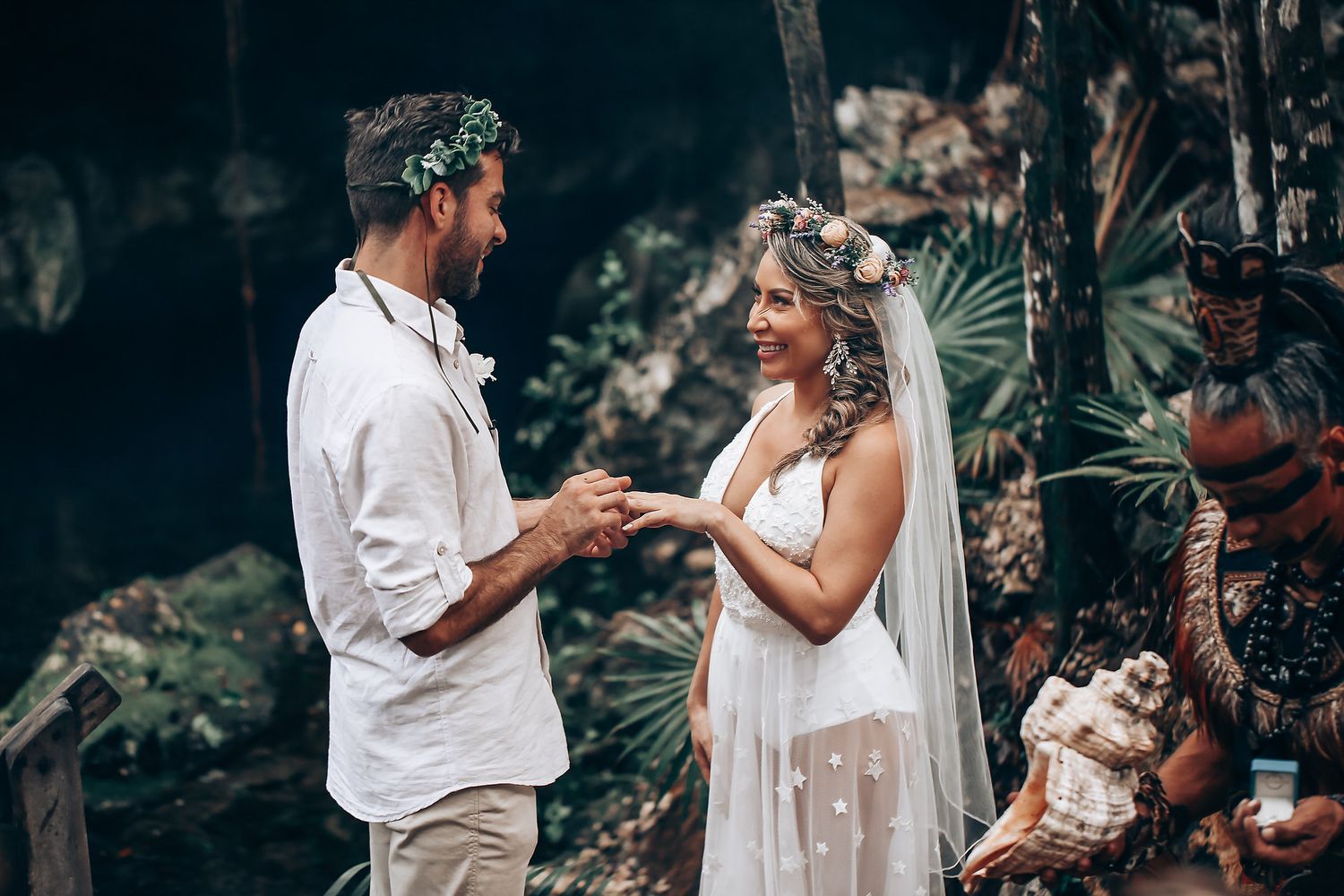 A couple shares an intimate moment during their wedding ceremony in a lush forest setting.