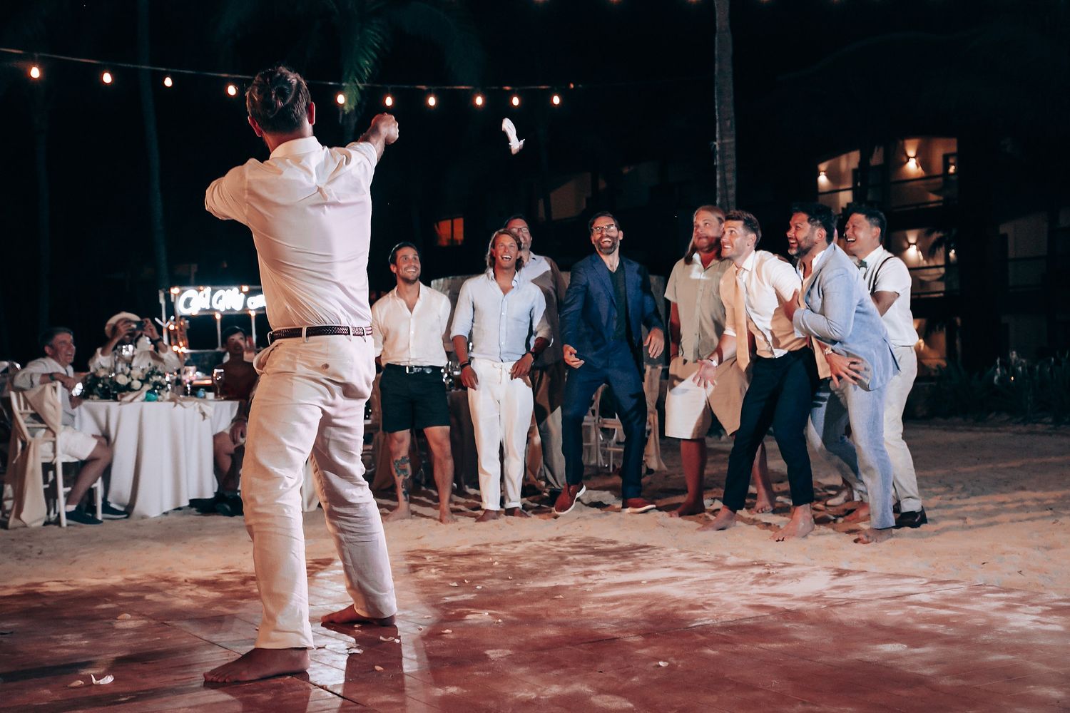 Wedding guests dancing on an outdoor dance floor at night with string lights overhead.
