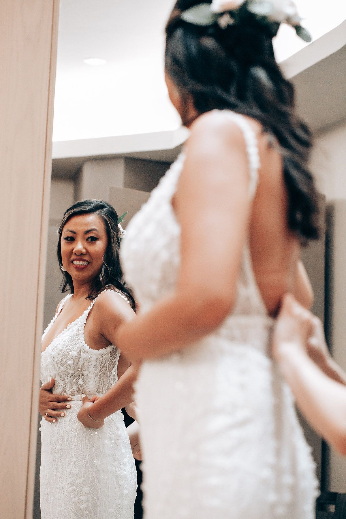 Bride looking at her reflection in a mirror while trying on a white lace wedding dress.