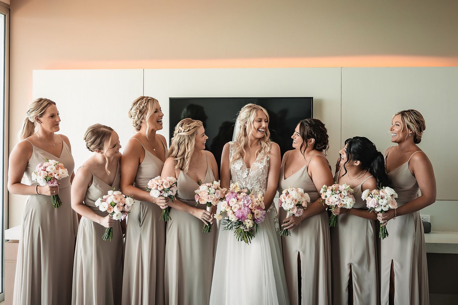 Wedding party lined up holding pink and white bouquets against neutral wall background.