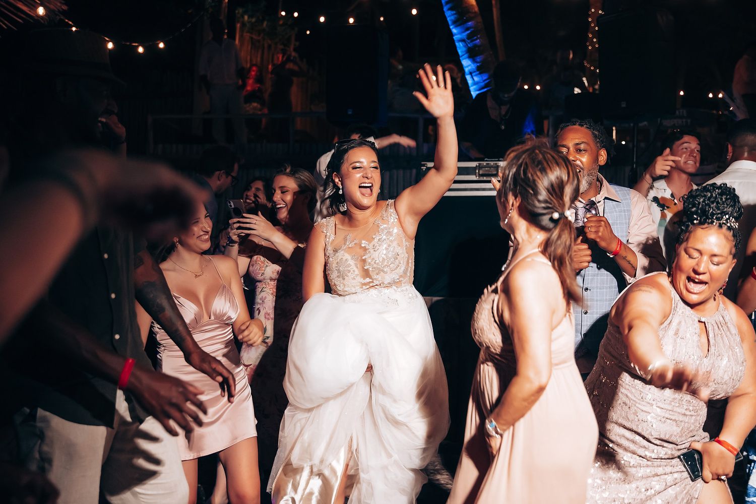 Wedding guests dancing and celebrating during nighttime reception with festive lighting.