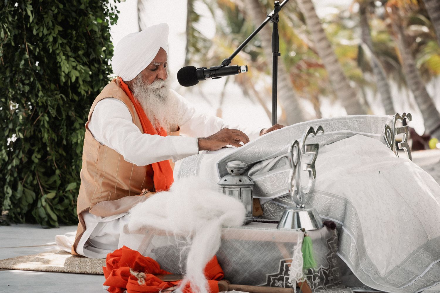 Elderly Sikh priest with white beard performs religious ceremony outdoors at traditional Punjabi wedding.