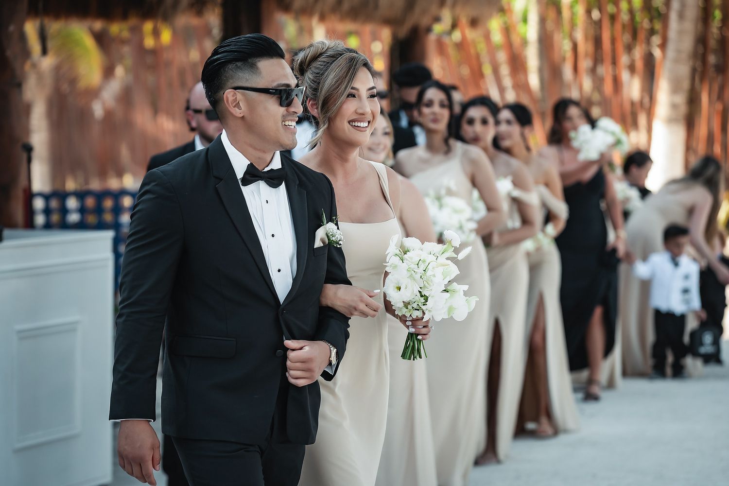 Bride and groom walk down the aisle with bridesmaids in champagne gowns at an elegant outdoor wedding ceremony.