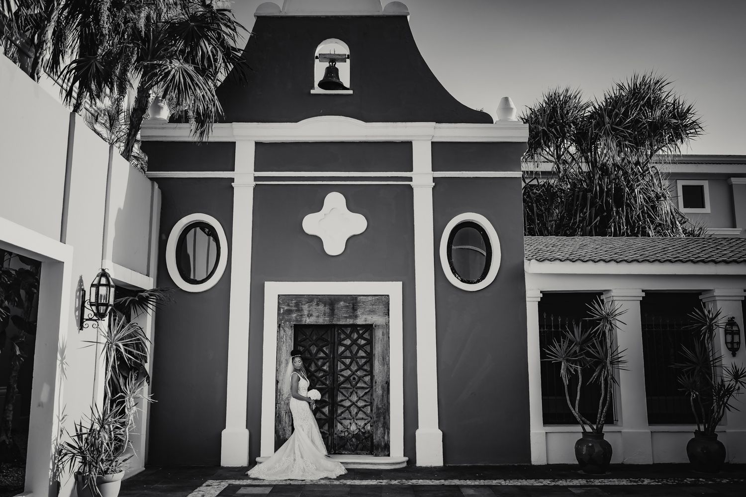 Black and white photo of a bride posing in front of a stunning colonial-style chapel with ornate details.