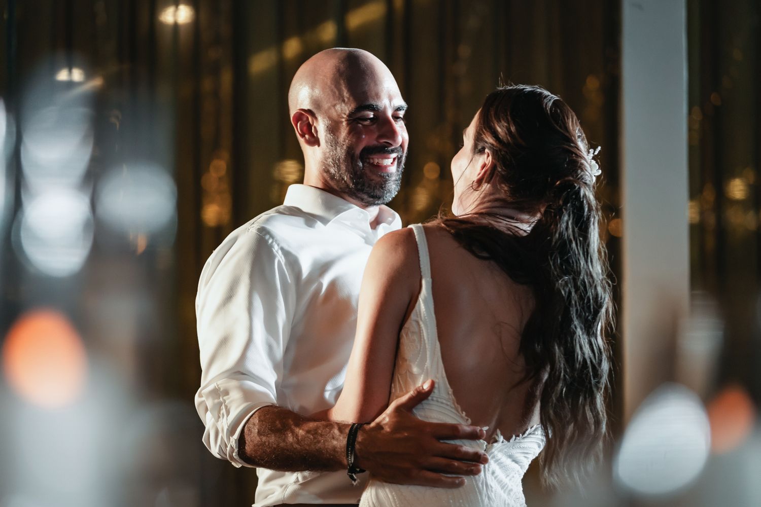 A smiling couple shares a romantic dance, the man in a white shirt embracing a woman in a backless dress.