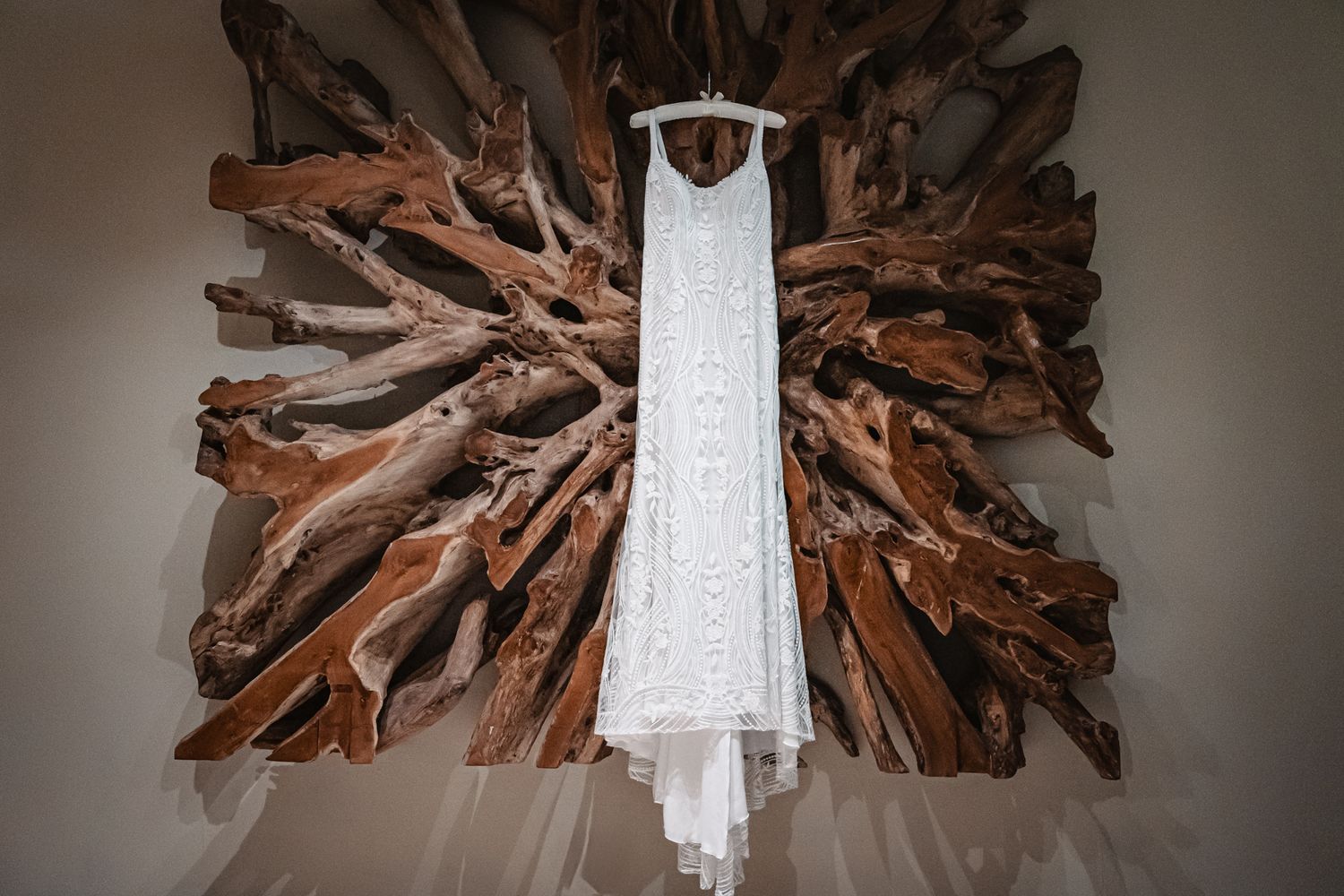White lace wedding dress hanging on rustic driftwood wall art display in elegant bridal preparation setting.