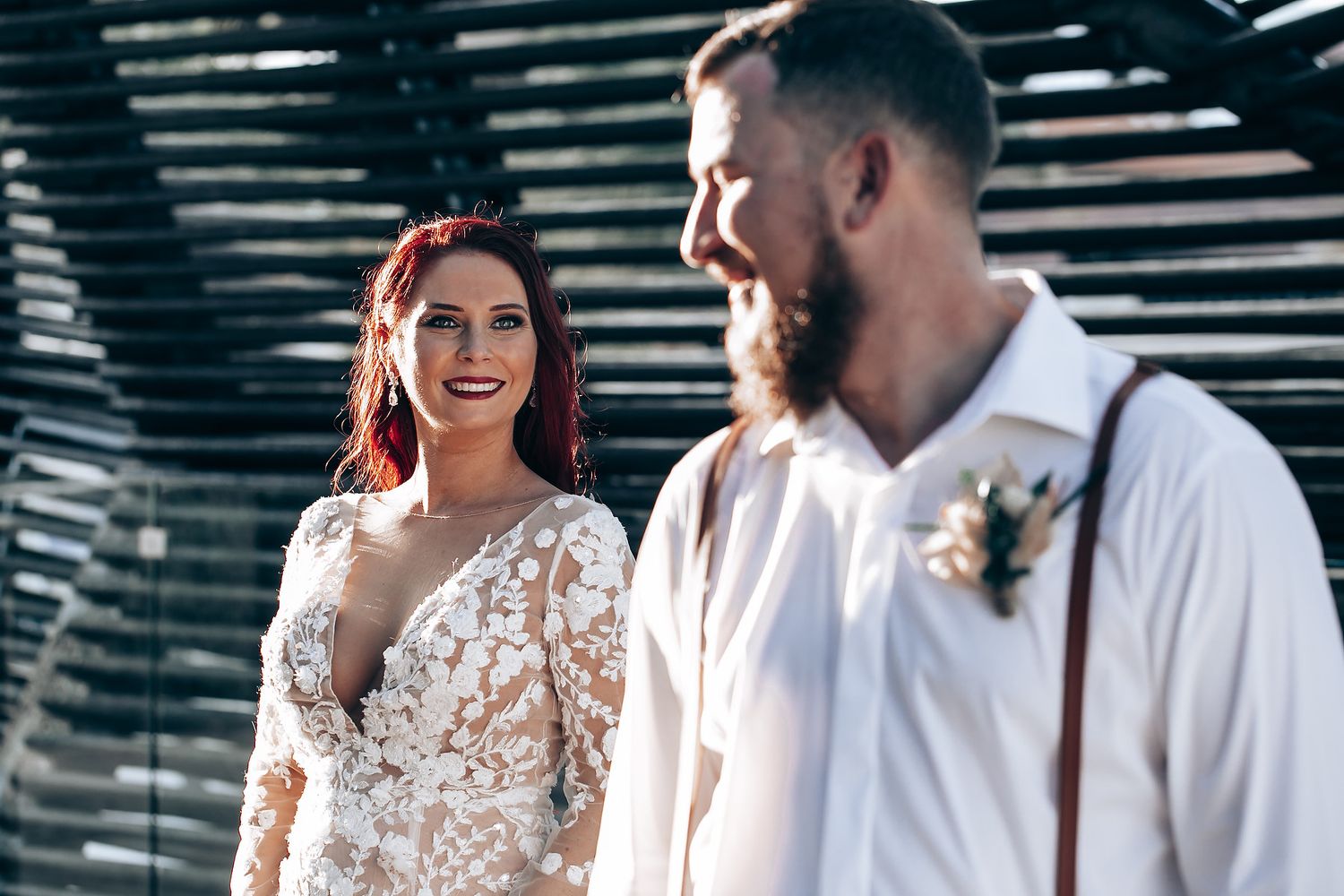 Intimate wedding moment captured under wooden pergola with natural lighting.