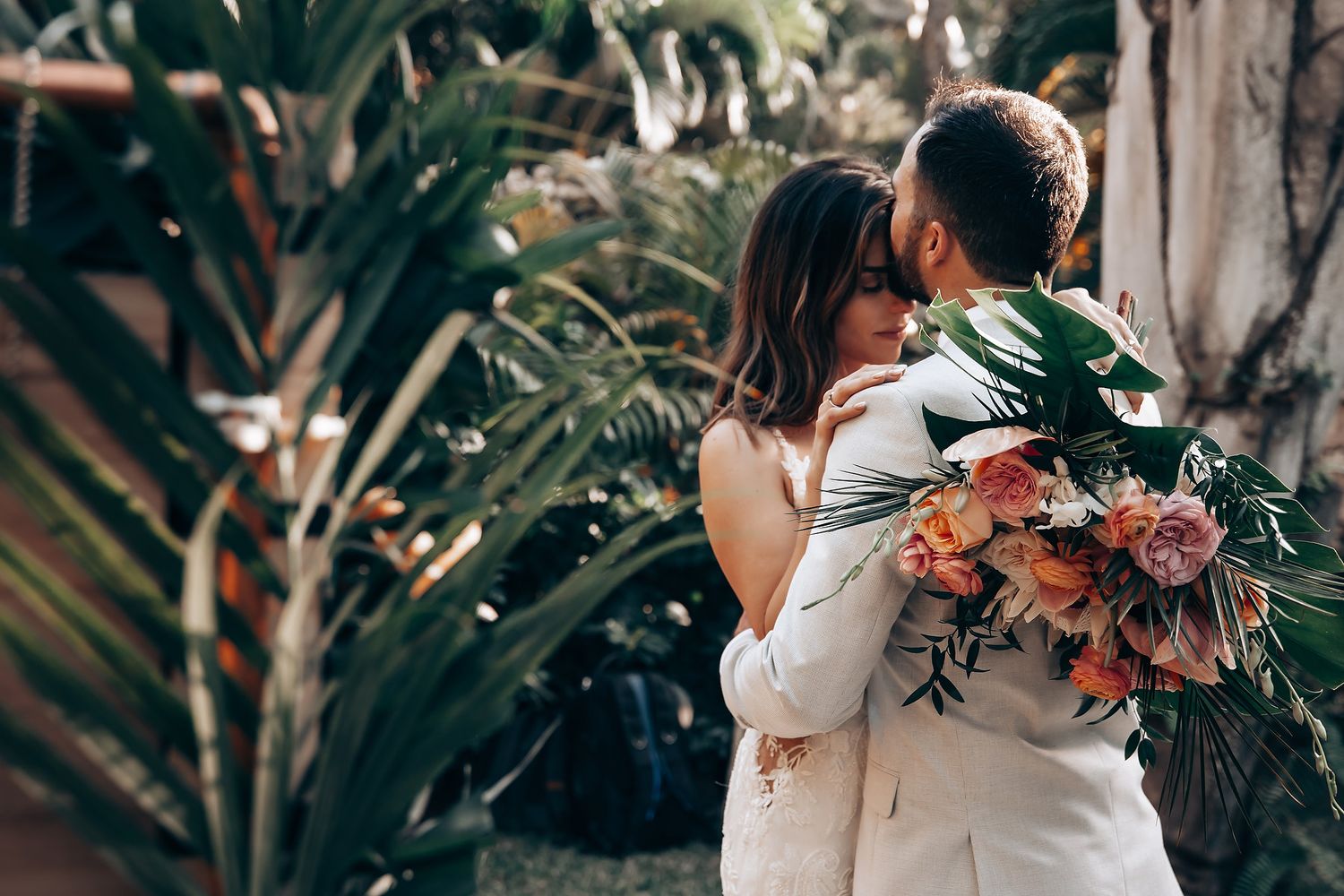 Wedding ceremony with coral and peach floral arrangements against tropical foliage backdrop.