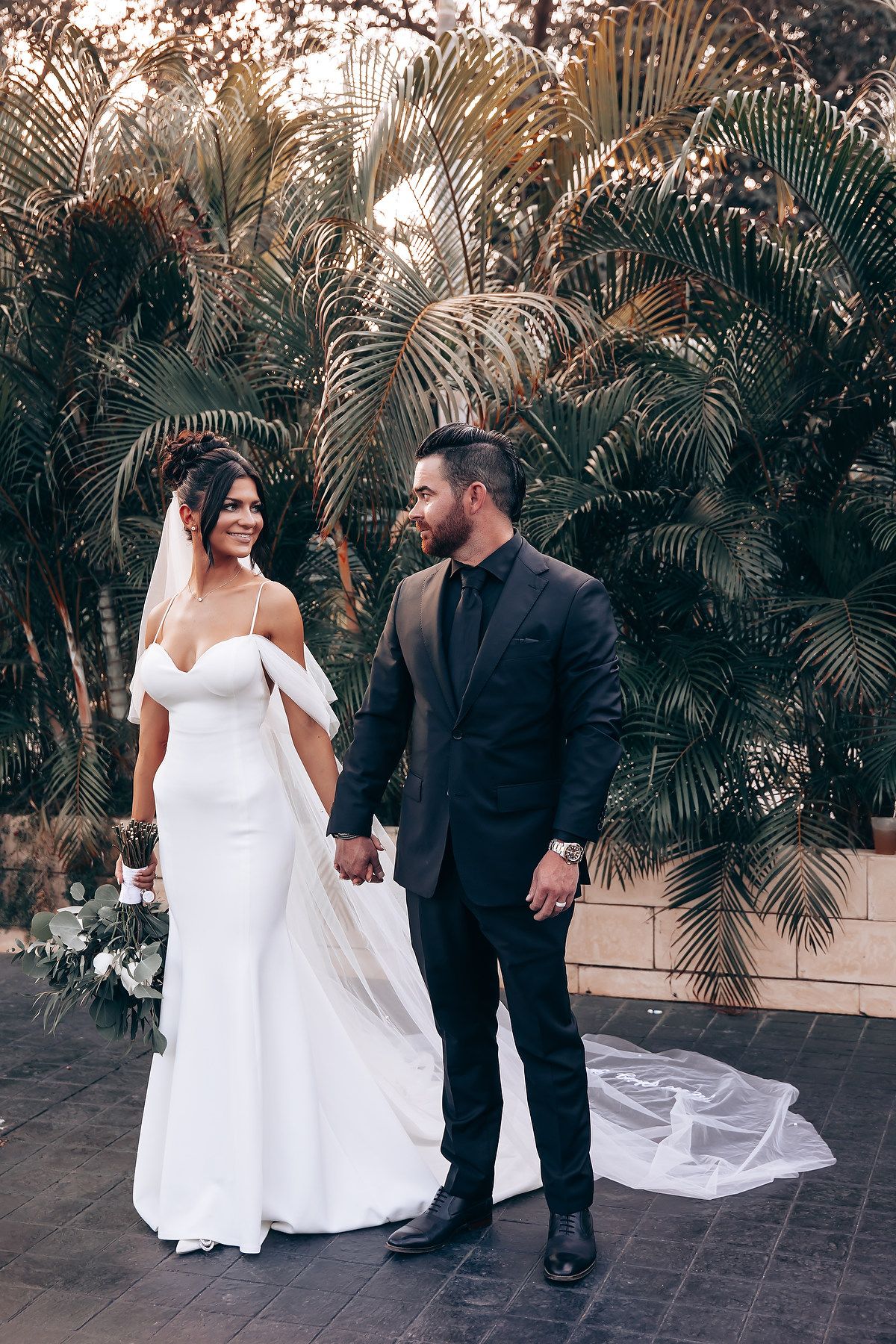 Wedding couple posing for photos among palm trees on stone patio.