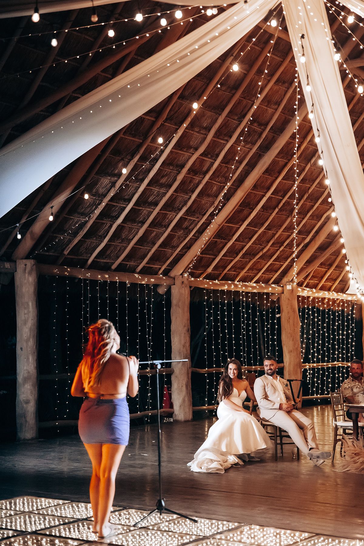A rustic barn venue decorated with string lights shows people dancing and celebrating at a wedding reception.