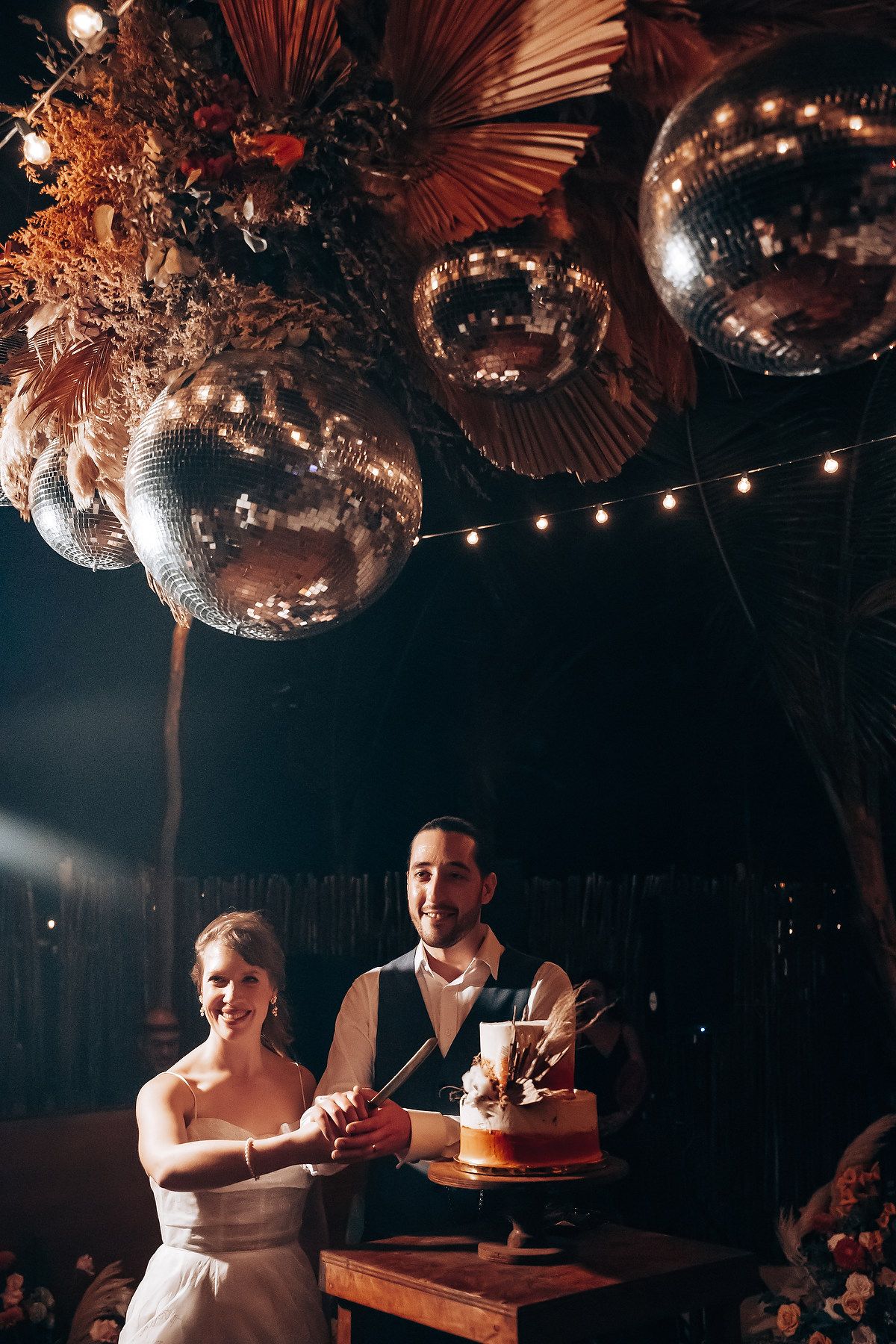 Intimate wedding reception setting with hanging disco balls and string lights creating moody atmosphere.