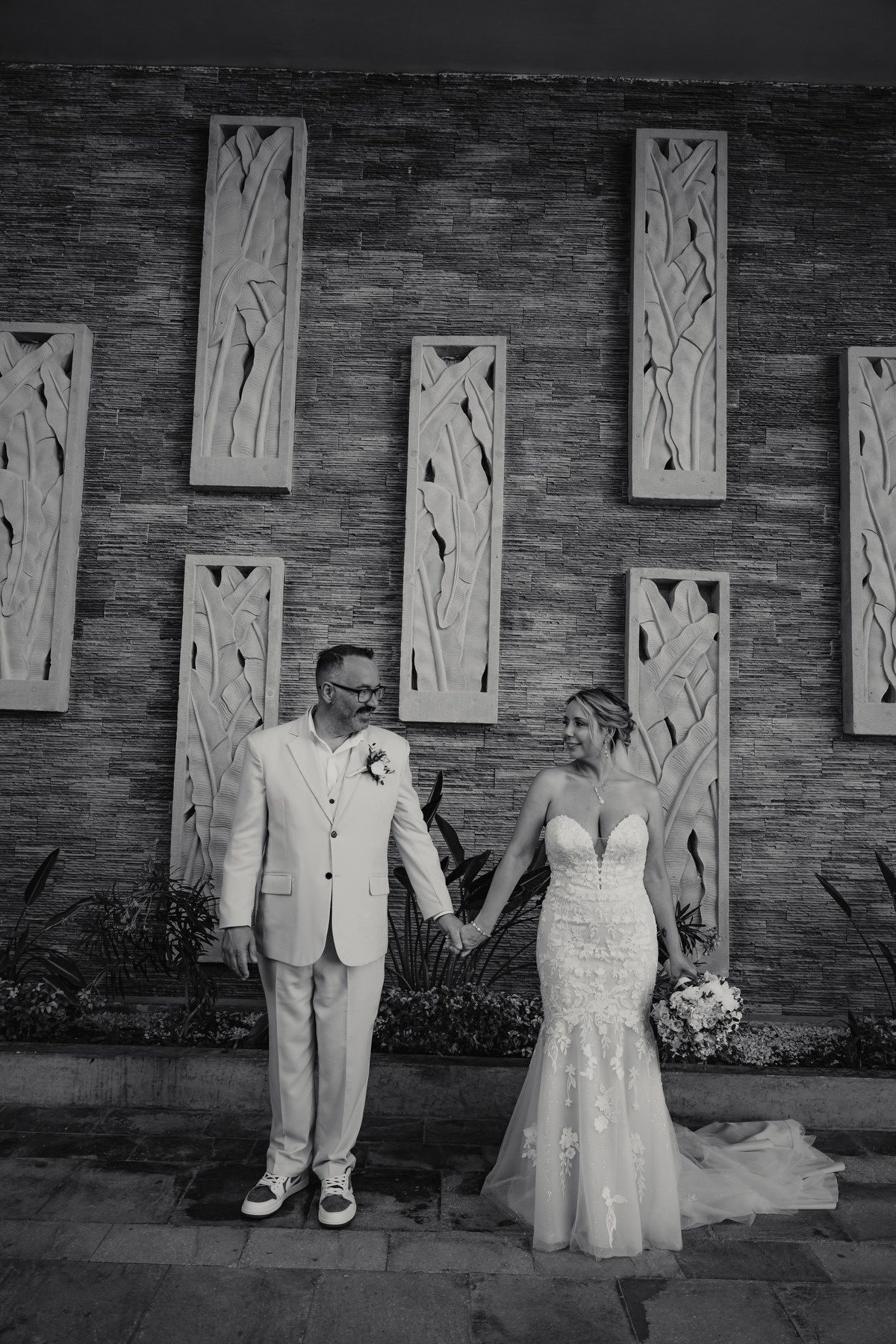 Black and white photo of bride and groom holding hands before decorative wall panels on their wedding day.