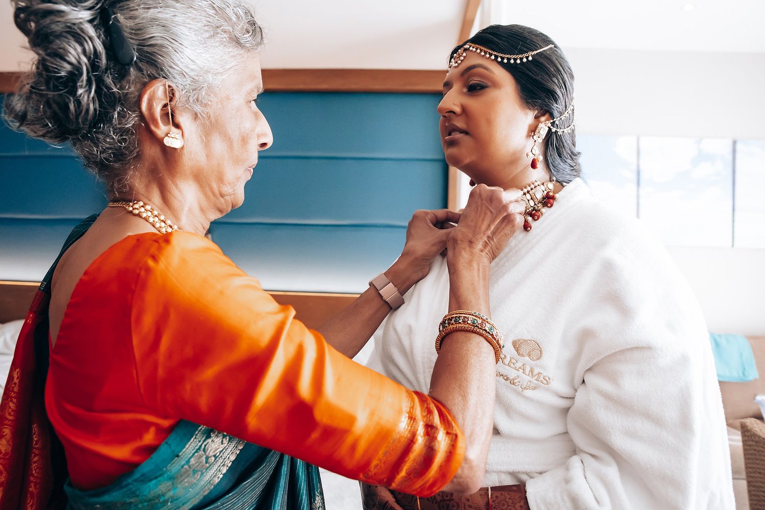 Traditional Indian wedding preparation with jewelry and blessings being given in vibrant orange and white attire.