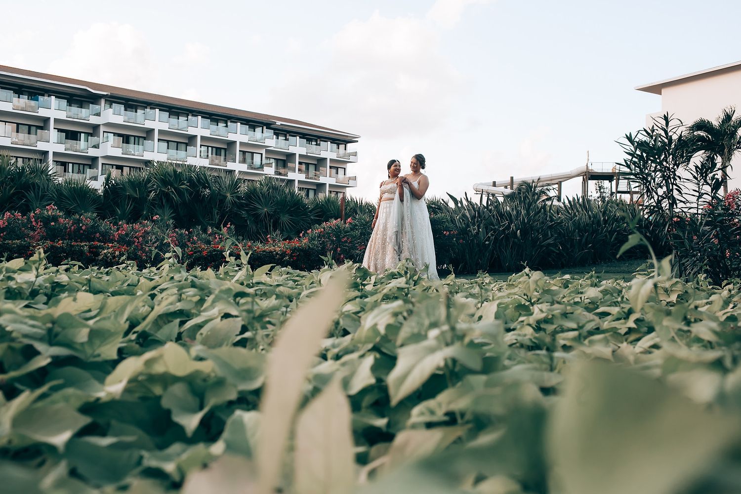 Couple walking through tropical garden with resort building in background.