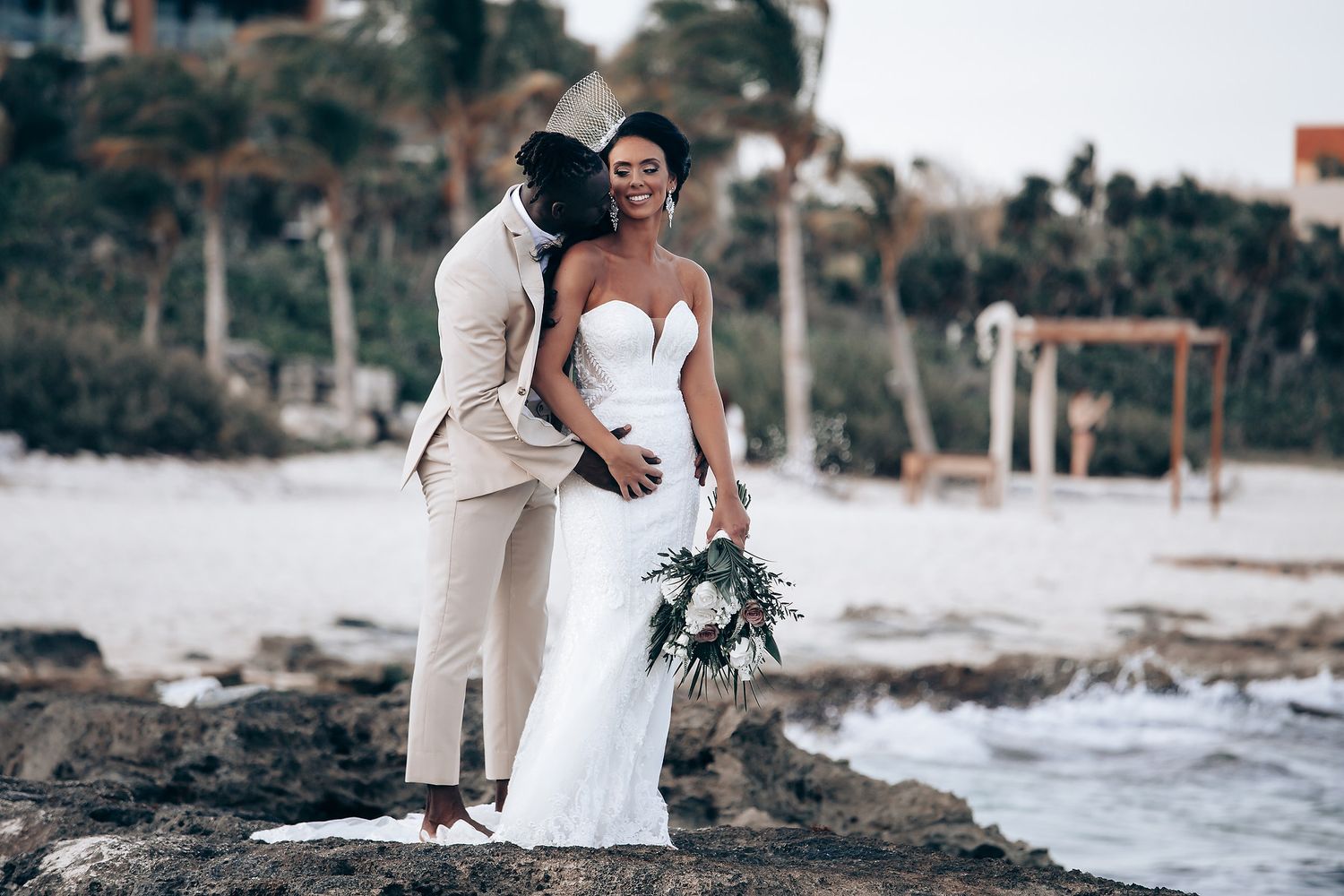 Beachside wedding celebration with palm trees and rocky coastline in the background.