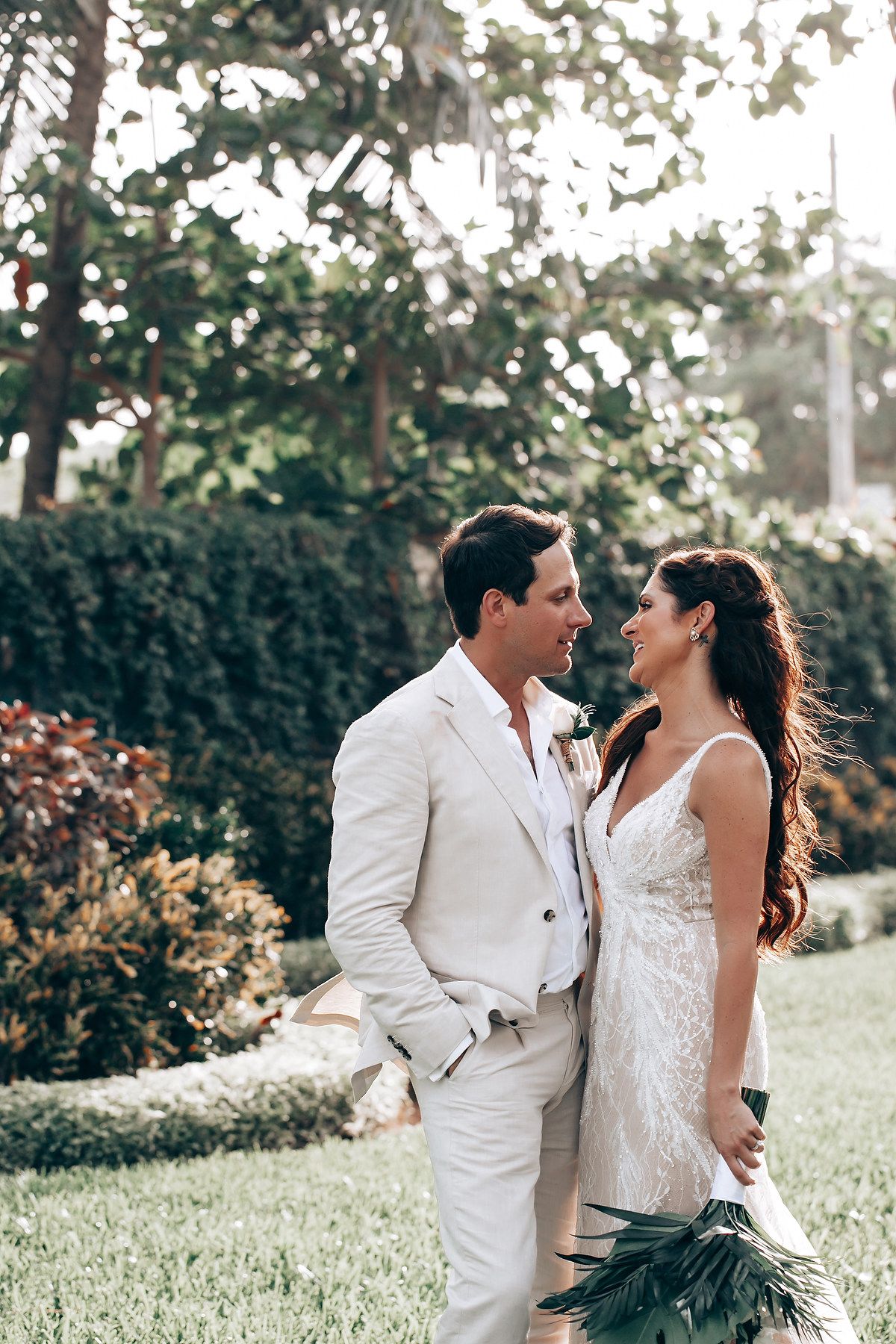 Romantic garden portrait of couple in white wedding attire holding tropical bouquet.