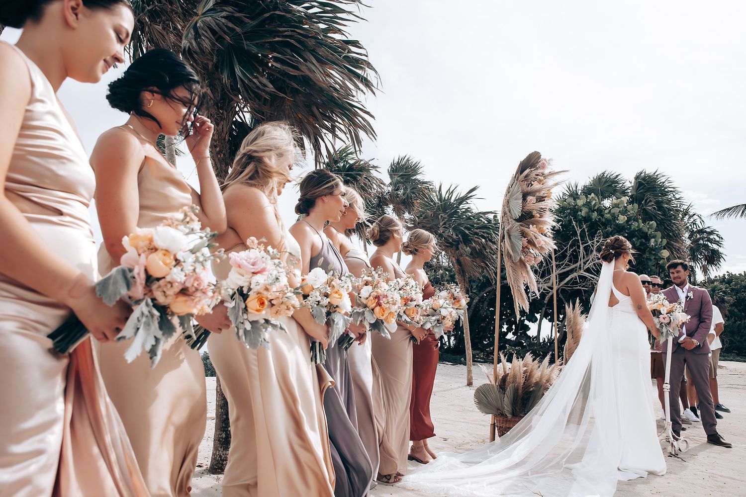 Wedding party posing together on a sunny beach with palm trees in the background.