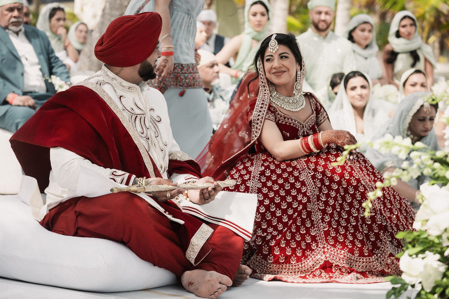 Bride and groom in red and white traditional Sikh attire sharing a moment during Anand Karaj ceremony.