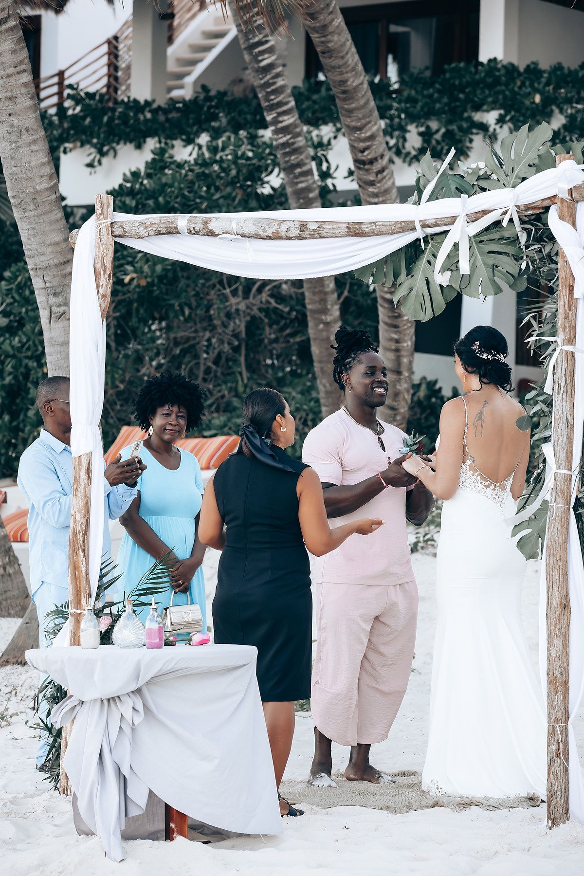 A couple stands under a decorated arch on a tropical beach.