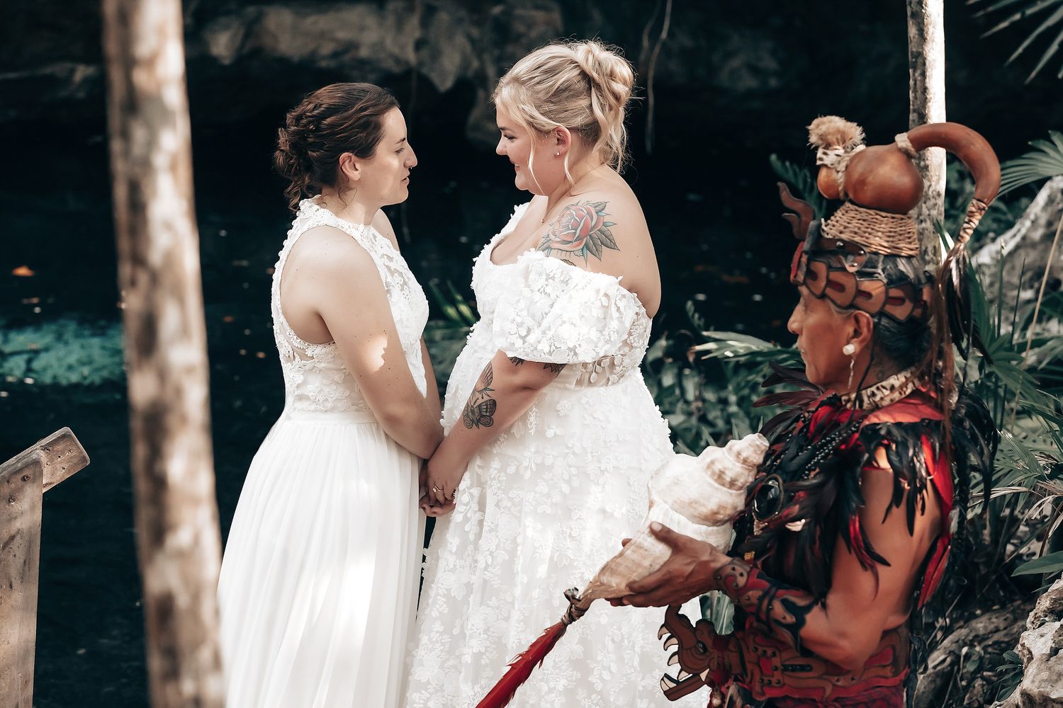 Two brides in white wedding dresses standing together in a garden.