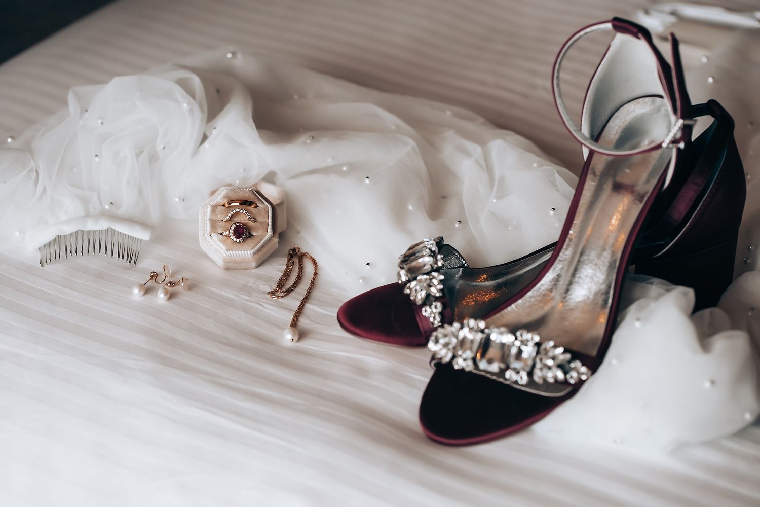 A pair of high-heeled shoes with rhinestone embellishments, surrounded by a white tulle veil and other wedding accessories.