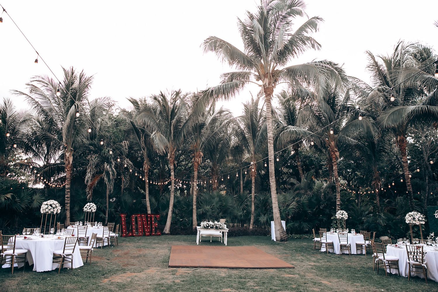 Outdoor wedding venue setup with white chairs and palm trees along a scenic pathway.