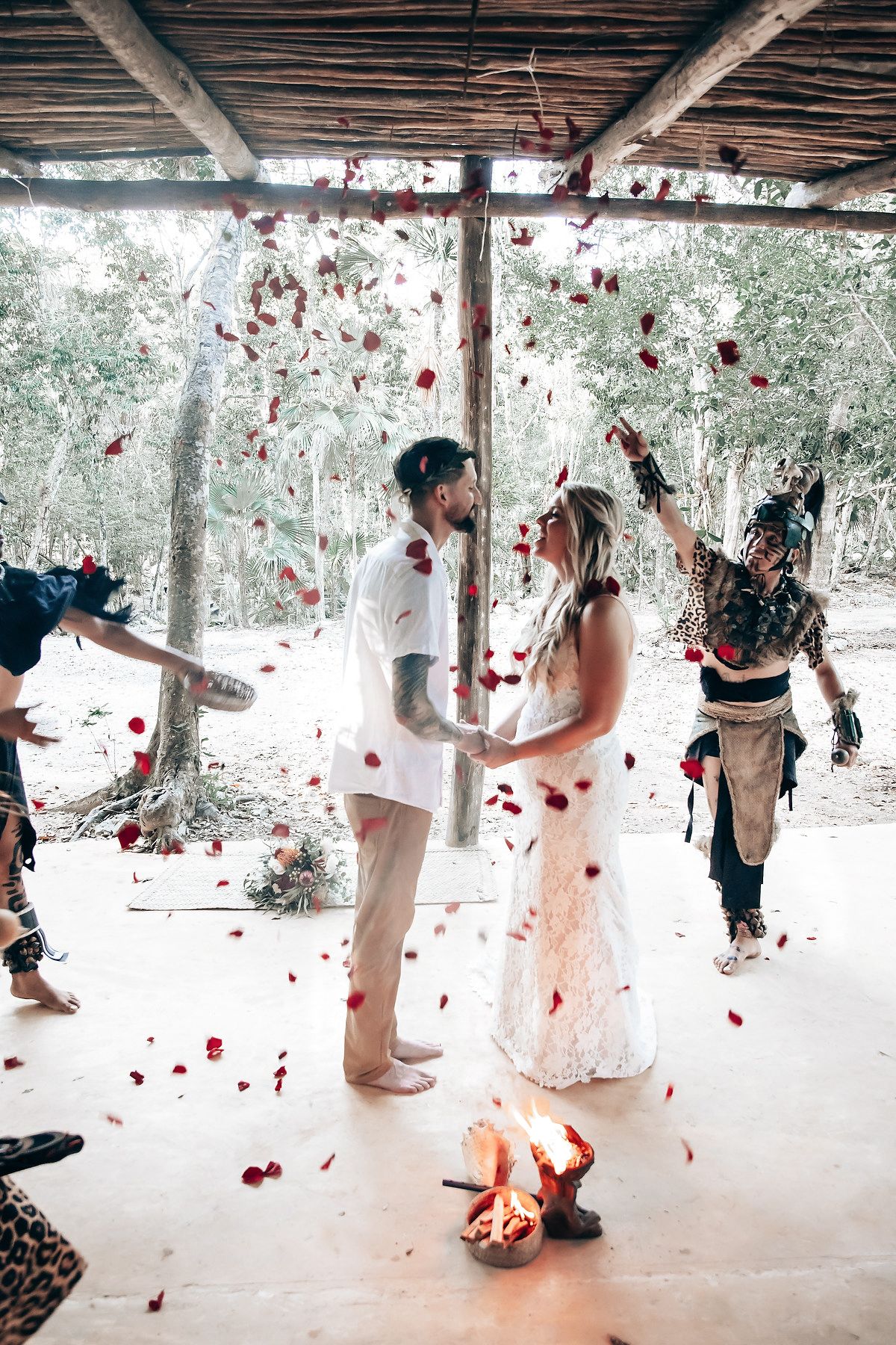 Falling rose petals create a romantic atmosphere as people celebrate under a rustic wooden pergola.