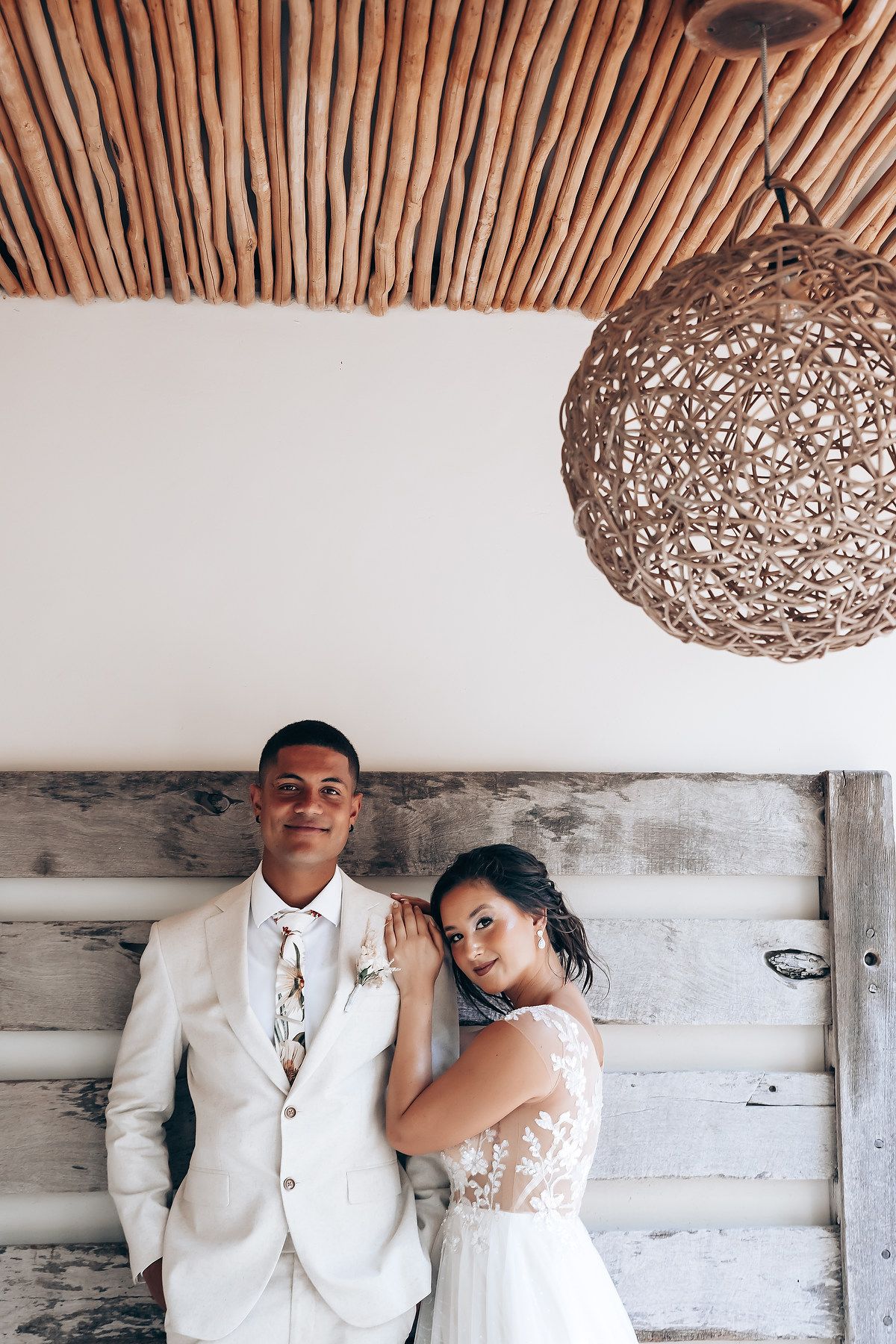 Newlyweds pose under rustic wooden ceiling with woven pendant light.
