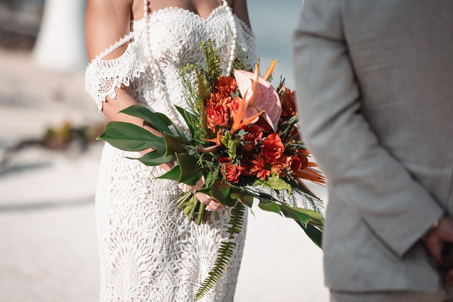 Close-up of bride holding vibrant tropical wedding bouquet with red and orange flowers.