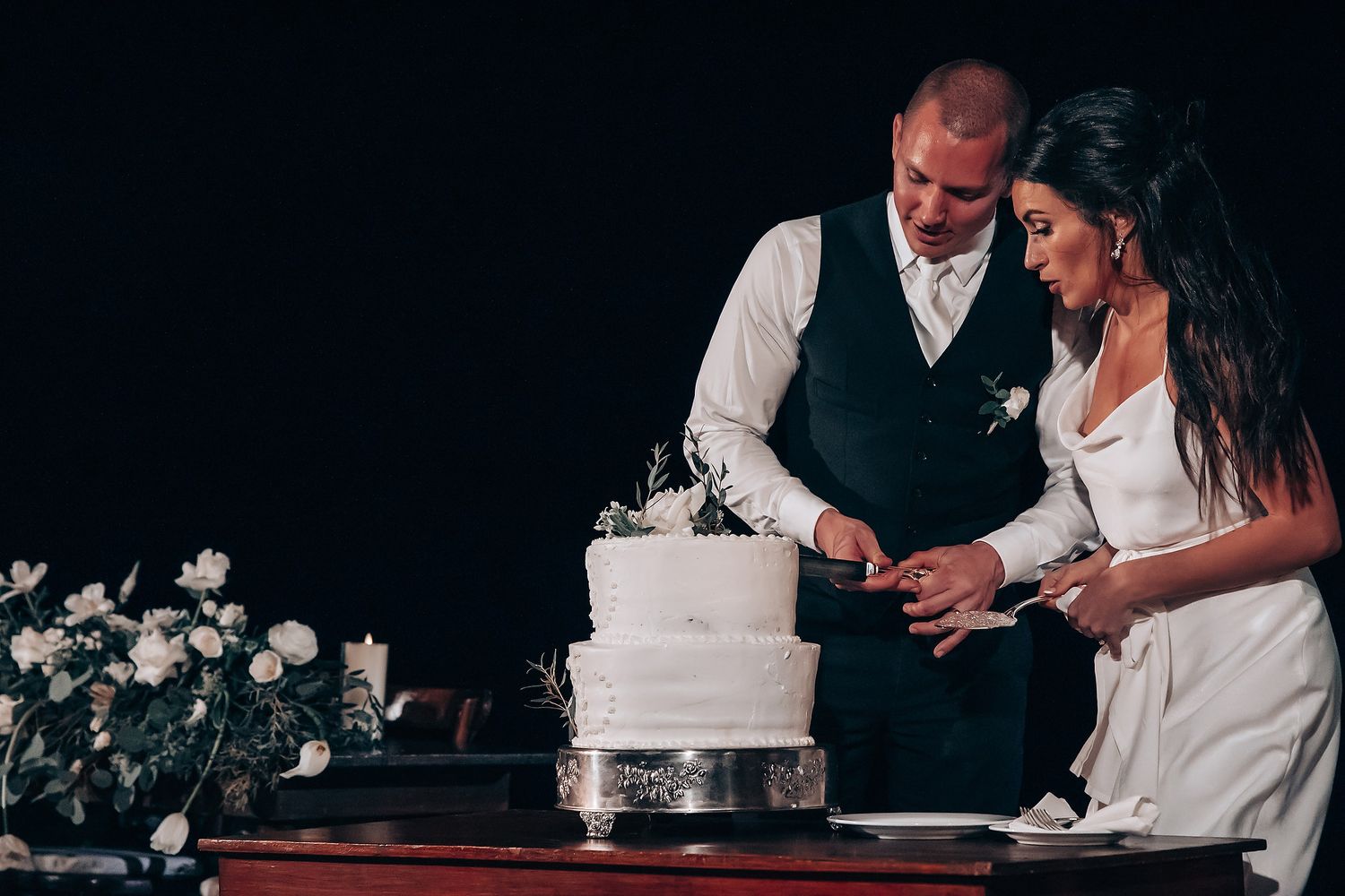 Wedding cake cutting ceremony in a dimly lit reception venue with decorative lights.