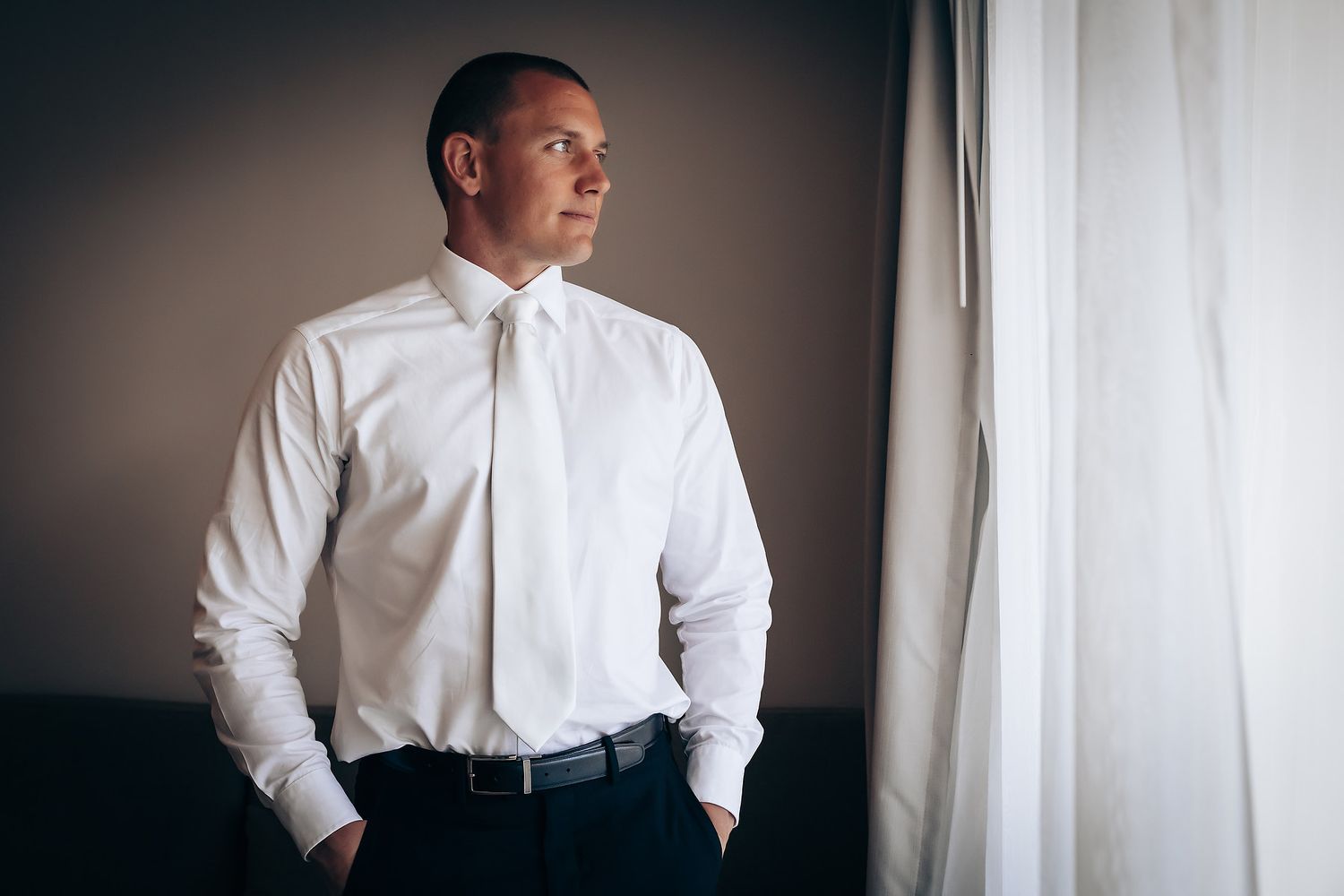A person in formal attire gazes thoughtfully out a window.