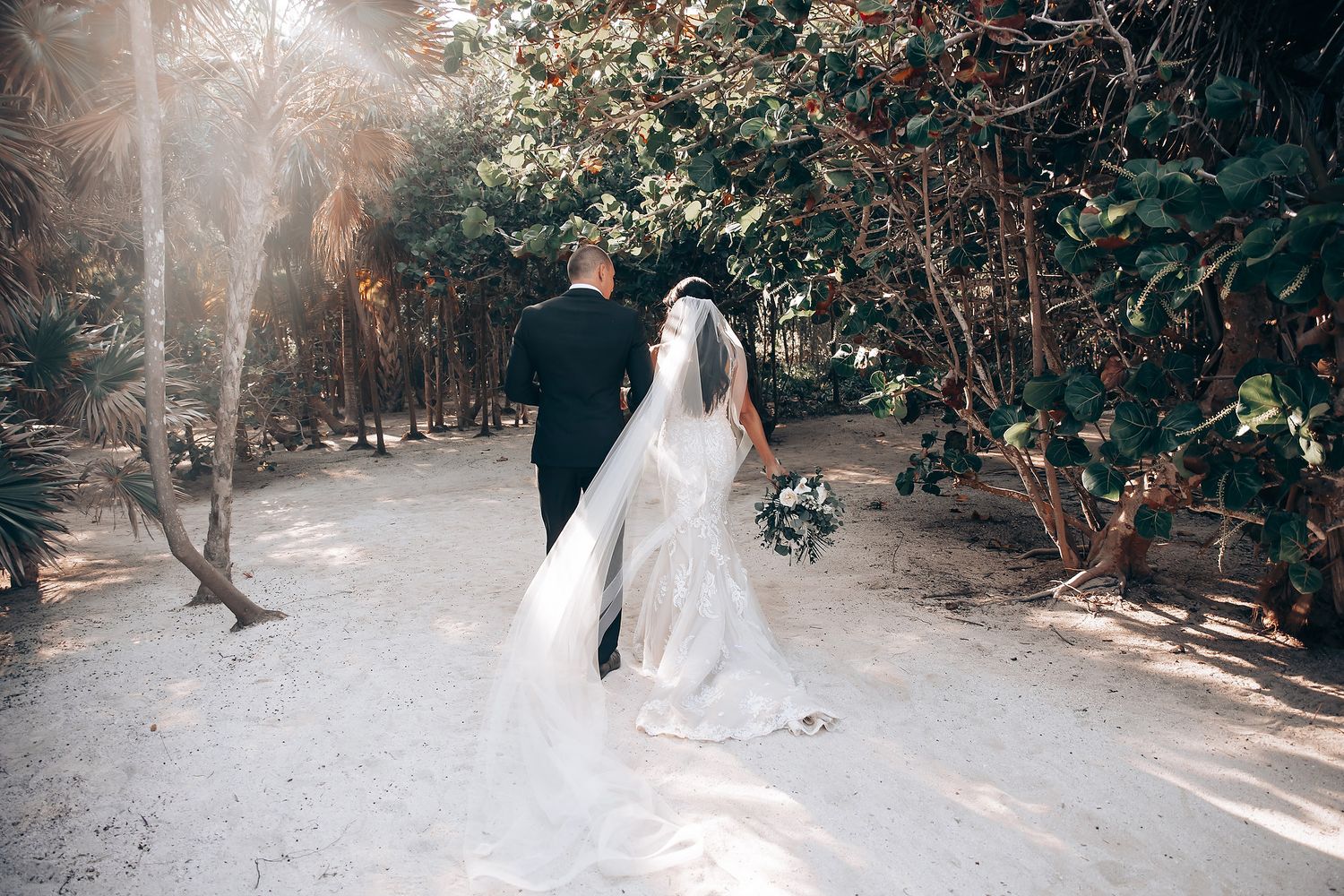 Wedding ceremony guests forming a tunnel outdoors in a wooded setting with natural sunlight filtering through.